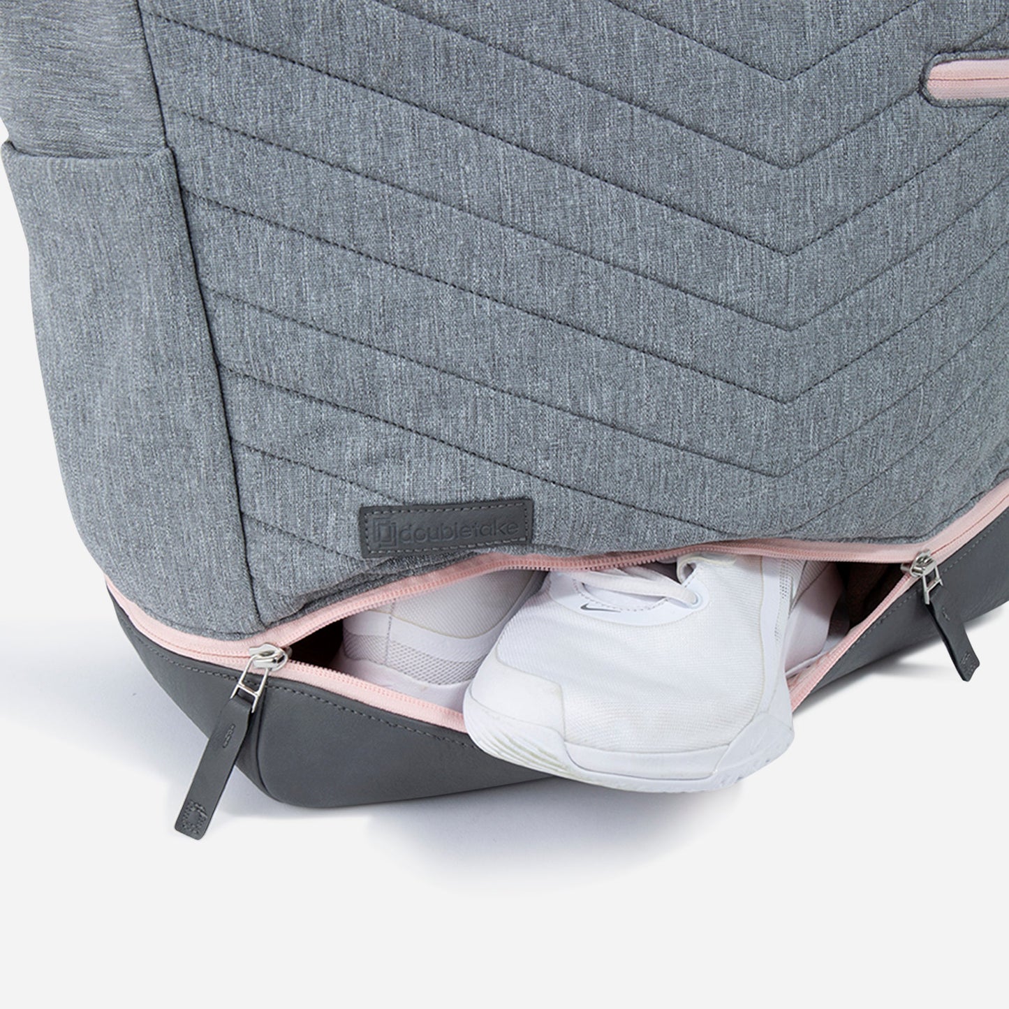 A close-up of the gray PARISII | Pickleball Tote by Doubletake with pink trim shows a zippered bottom compartment partially open, neatly storing white sneakers. The tote is ideal for pickleball and features the Doubletake brand on a small gray label.