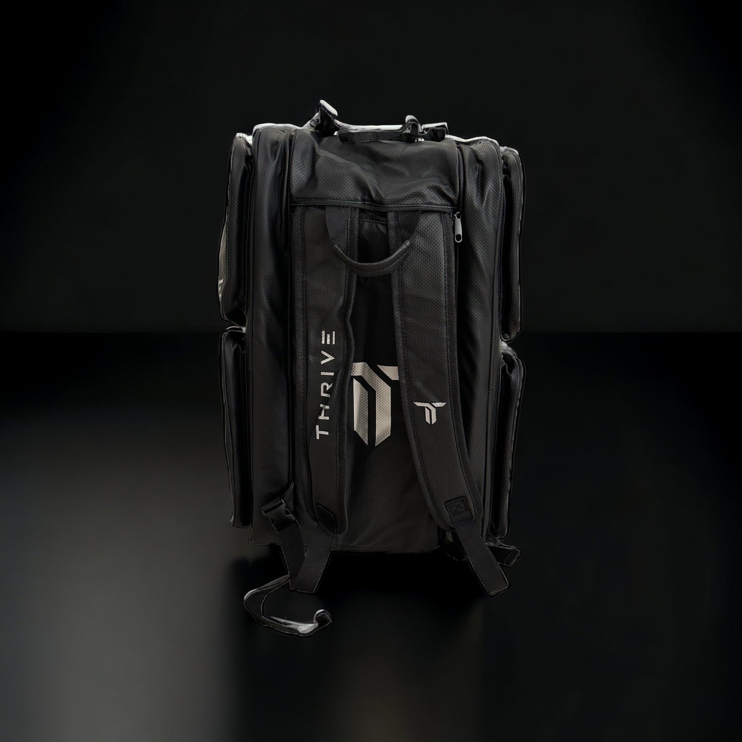 The Elite Pro Tour Bag w/shoe bag- BLACK by Thrive Pickleball features vegan leather, thermal-lined paddle compartments, side pockets, padded straps, a top handle, plus a white THRIVE geometric logo on the back. Displayed upright on a black surface.