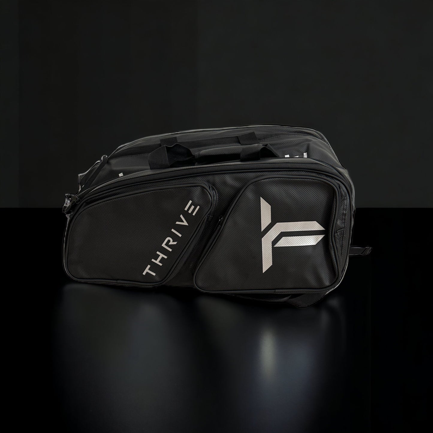 The Elite Pro Tour Bag w/shoe bag- BLACK by Thrive Pickleball is a sleek vegan leather duffel with "THRIVE" in white on one pocket, a silver logo on another, two handles, thermal-lined paddle compartments, and multiple zip pockets.