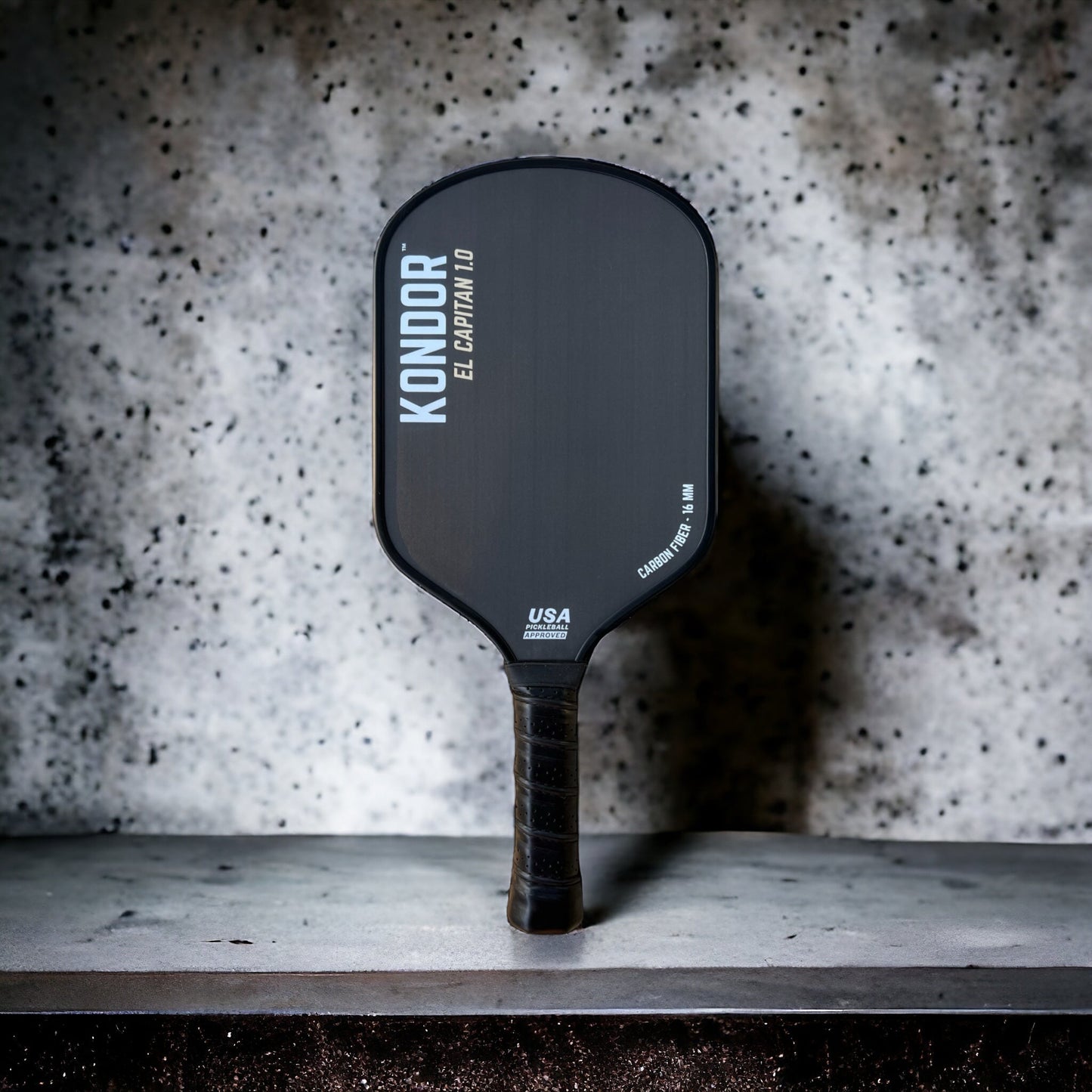 The El Capitán 1.0 by KONDOR PICKLEBALL rests on the counter, showcasing its honeycomb core and extended energy grip for enhanced control.