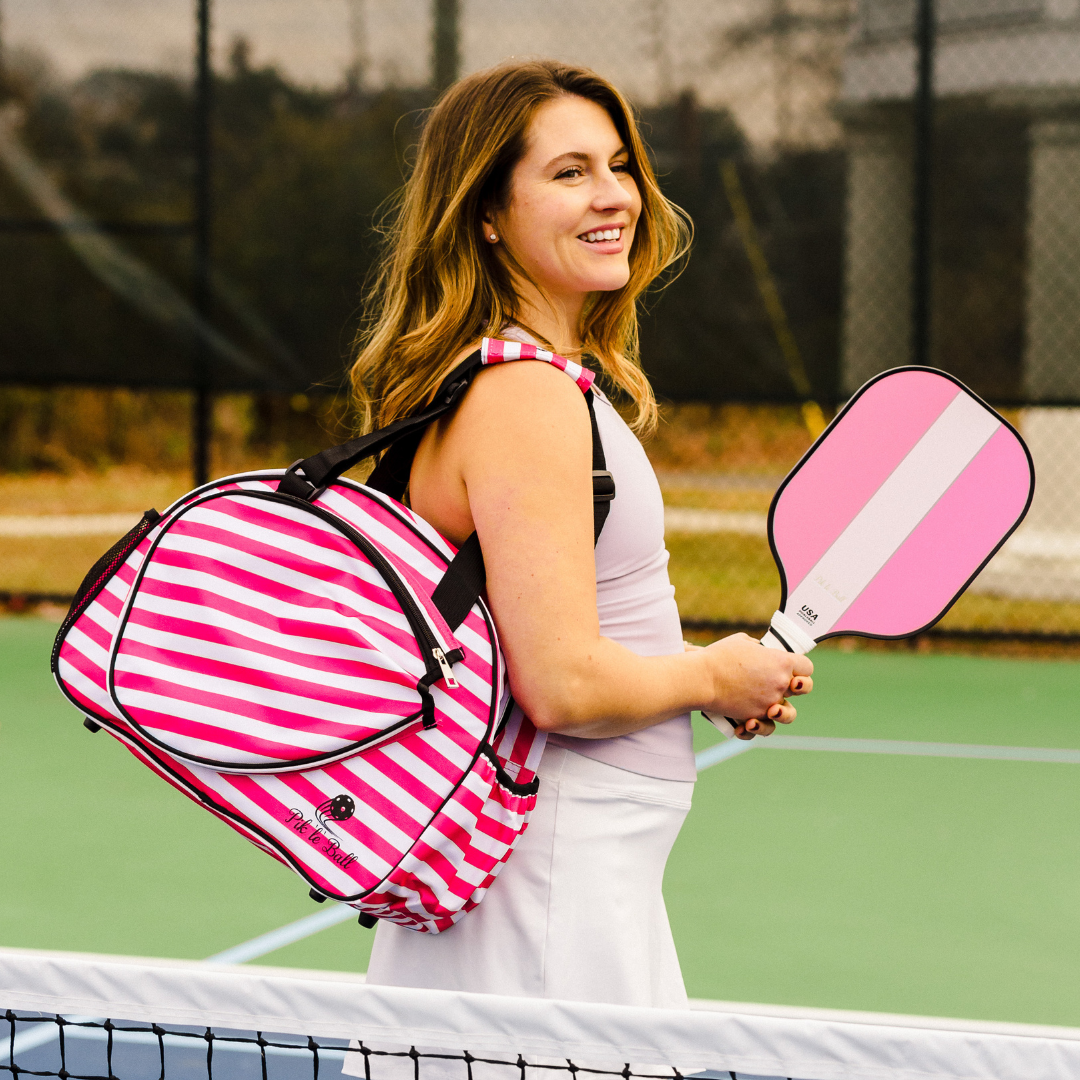 A woman stands ready for the court beside the Pik'le'Ball Sports Stylish Stripe Pink Premium Women's Pickleball Bag.