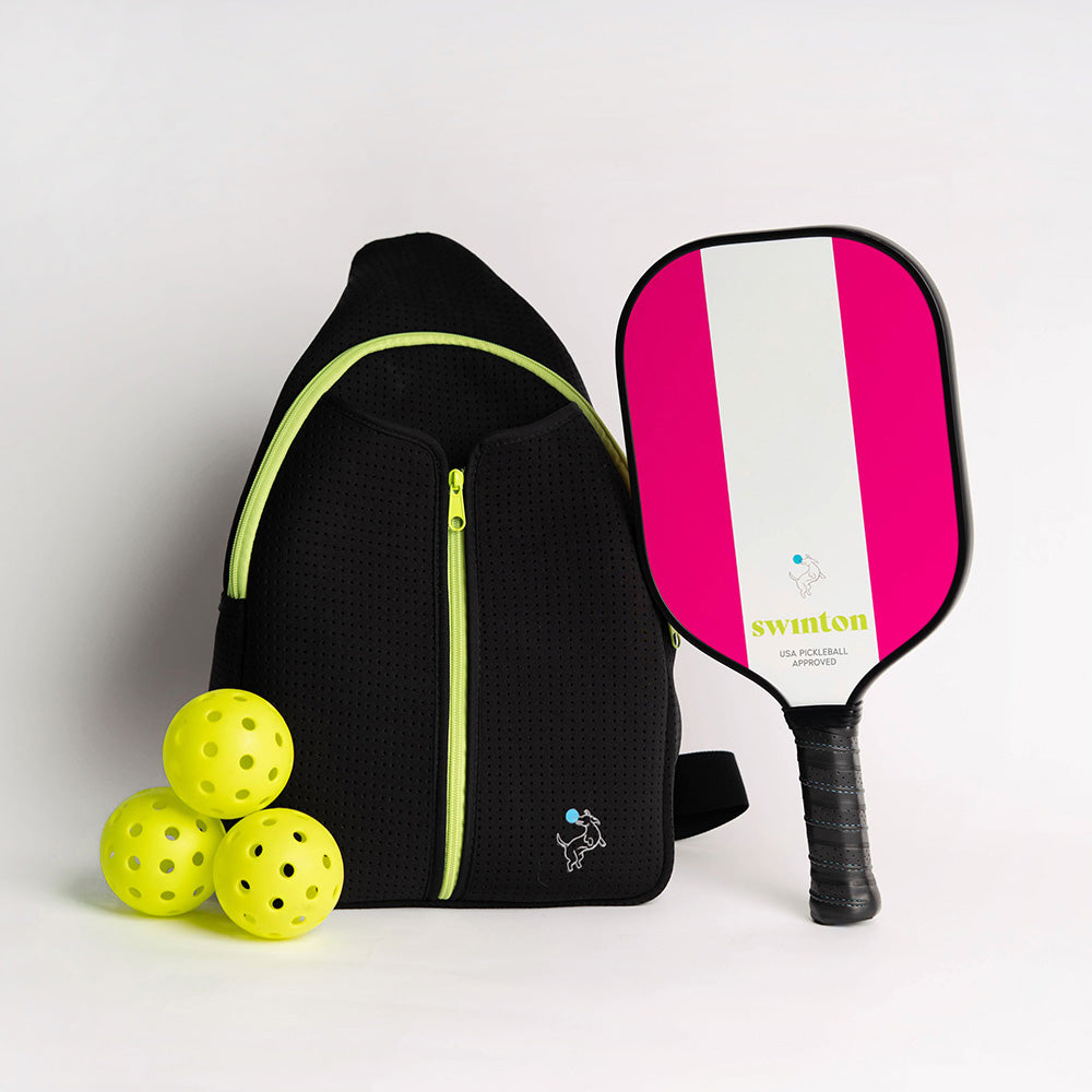 A black backpack with lime green zippers sits next to a Swinton Pickleball Hero Pink Stripe paddle, USA Pickleball Approved. Three yellow perforated pickleballs are in the foreground, set against a plain white background.