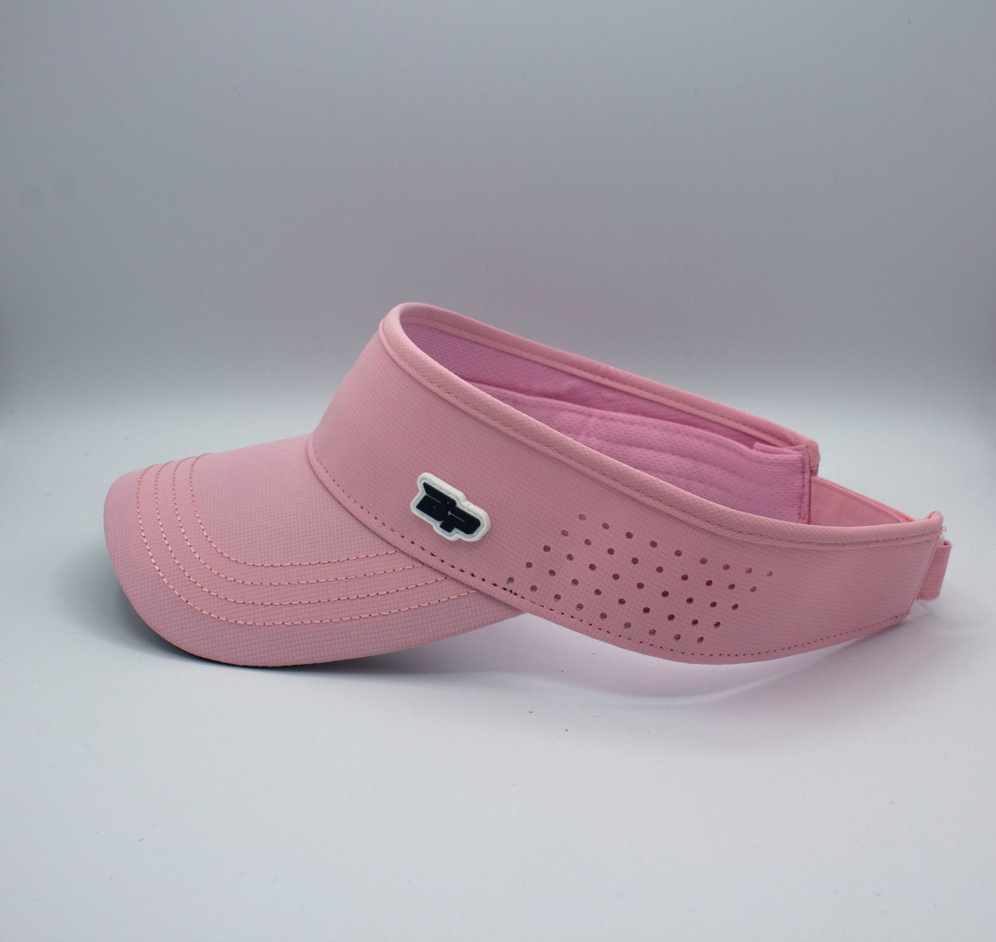 The Bodhi Performance ICON Visor is pink with a curved brim, small side ventilation holes, and a black and white logo on the front. Its plain white backdrop highlights the visor’s vibrant color and sporty design.