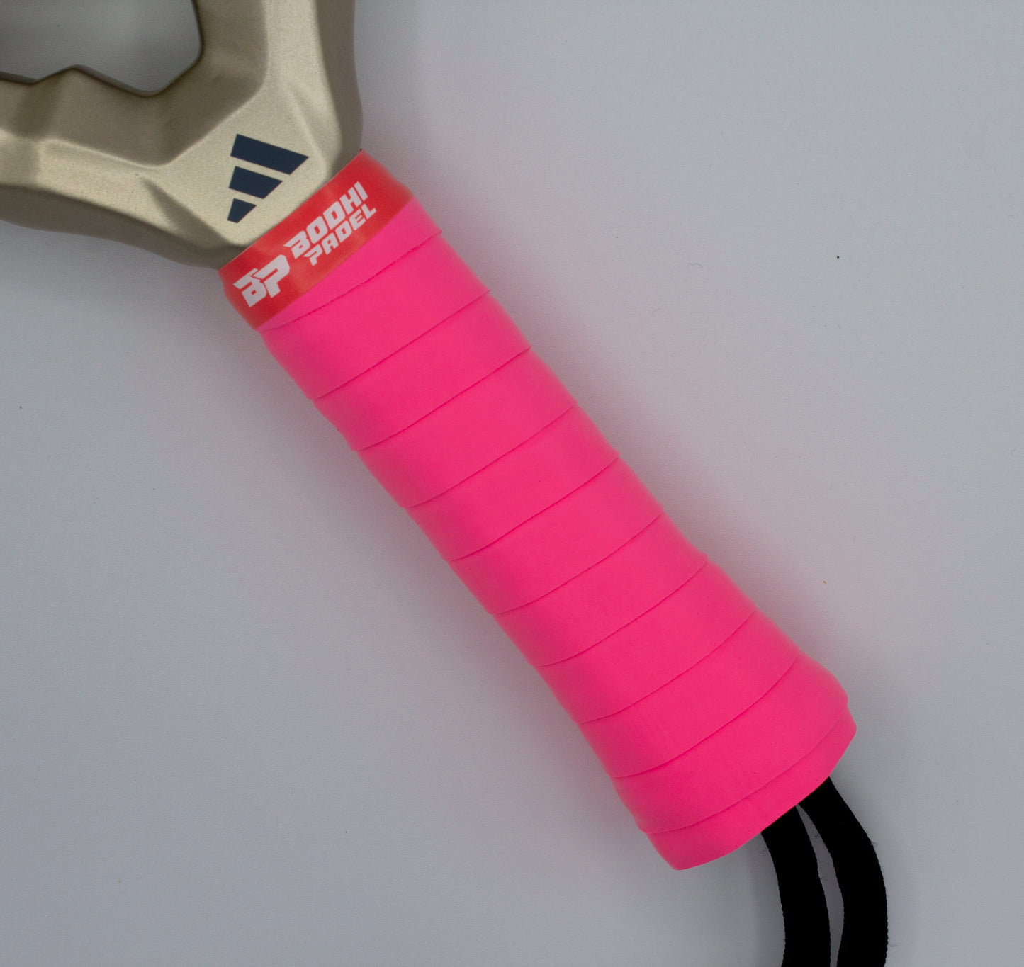 Close-up of a sports paddle handle wrapped in bright pink PROtack™ Premium Padel Overgrips by Bodhi Performance for superior moisture absorption. A metallic gold section shows a blue Adidas logo; below, "Zoom Padel" is on a white-on-red label. Light gray background.