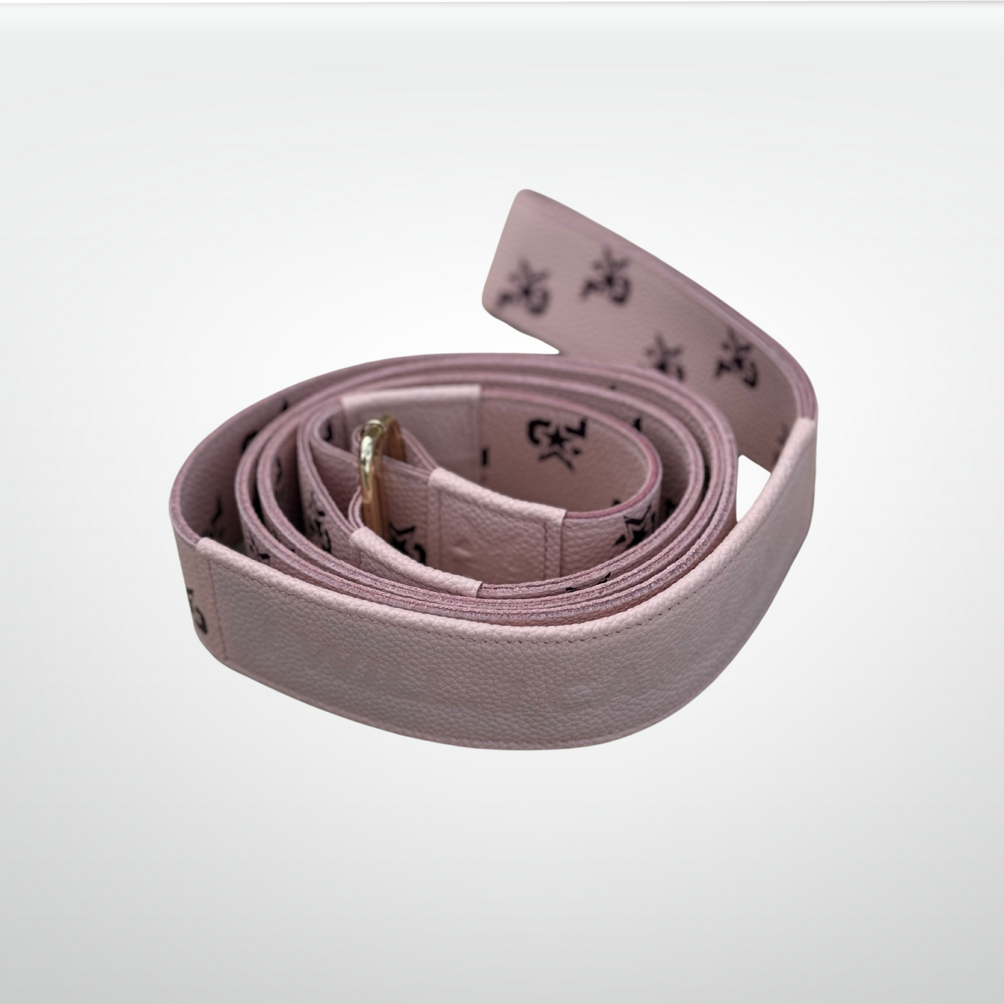 The iReliev I AM Leather Monogram Yoga Strap is a light pink leather accessory with a subtle texture, gold buckle, and black printed symbols. Its refined look and best-in-class style are highlighted against a plain white background.