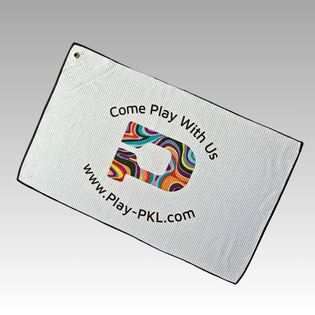 The Playly Store Two-Bounce Towel is a white microfiber waffle weave towel with black trim, featuring a colorful swirling P, “Come Play With Us” above, www.Play-PKL.com below, and a metal grommet for golf bag attachment.