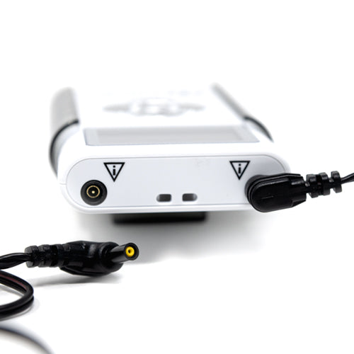 Close-up of an iReliev ET-8080 device with two black ports marked by warning triangles. An Extra Long TENS Lead Wire is plugged into one port, while another yellow-tipped cable lies nearby on a plain, blurred background.