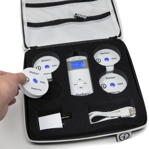 A hand lifts a round iReliev wireless pod from the Hard Protective Carry Case for Wireless TENS EMS, which holds four pods, a white remote, USB cable, and wall charger—each securely organized in their own slots. The case is partially unzipped.