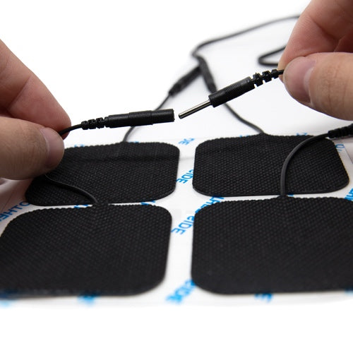 Close-up of hands connecting wires to iReliev TENS + EMS Pain Relief & Recovery System’s black electrode pads. Four adhesive pads rest on a backing sheet, with a plain, out-of-focus background.