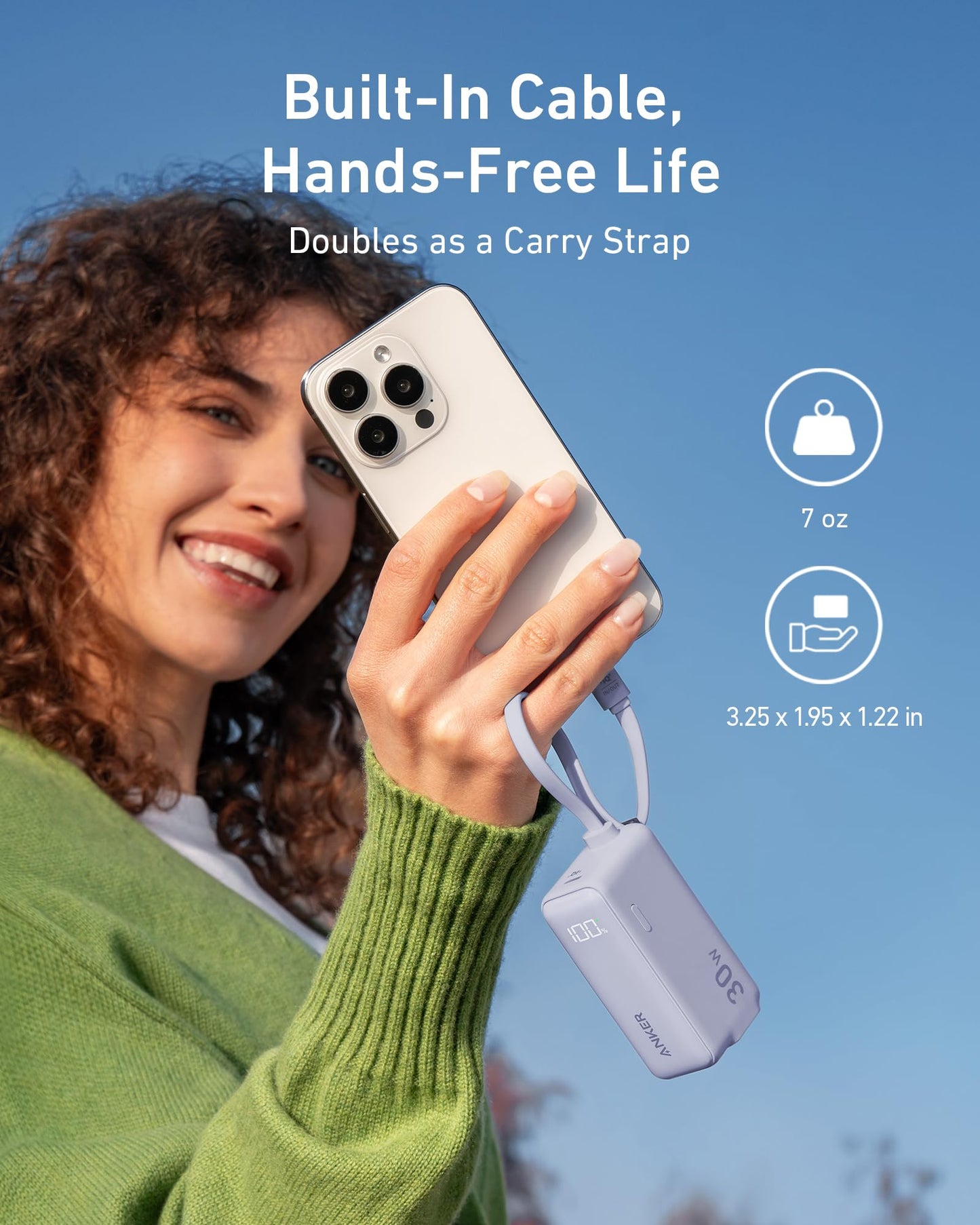 A smiling woman in a green sweater holds her smartphone with an Anker Power Bank (30W, 5k, Fusion, Built-In USB-C Cable) attached by a short strap. Text: “Built-In Cable, Hands-Free Life. Doubles as a Carry Strap.” Weight and size icons included.