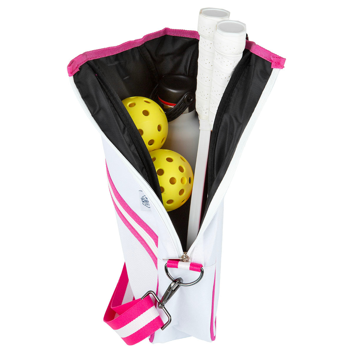 The Queen of the Court Essentials Pickleball Bag, shown upright against a white background, is open to reveal two yellow balls, two white-handled paddles, and a black water bottle inside. The bag features a stylish white and pink crossbody design.