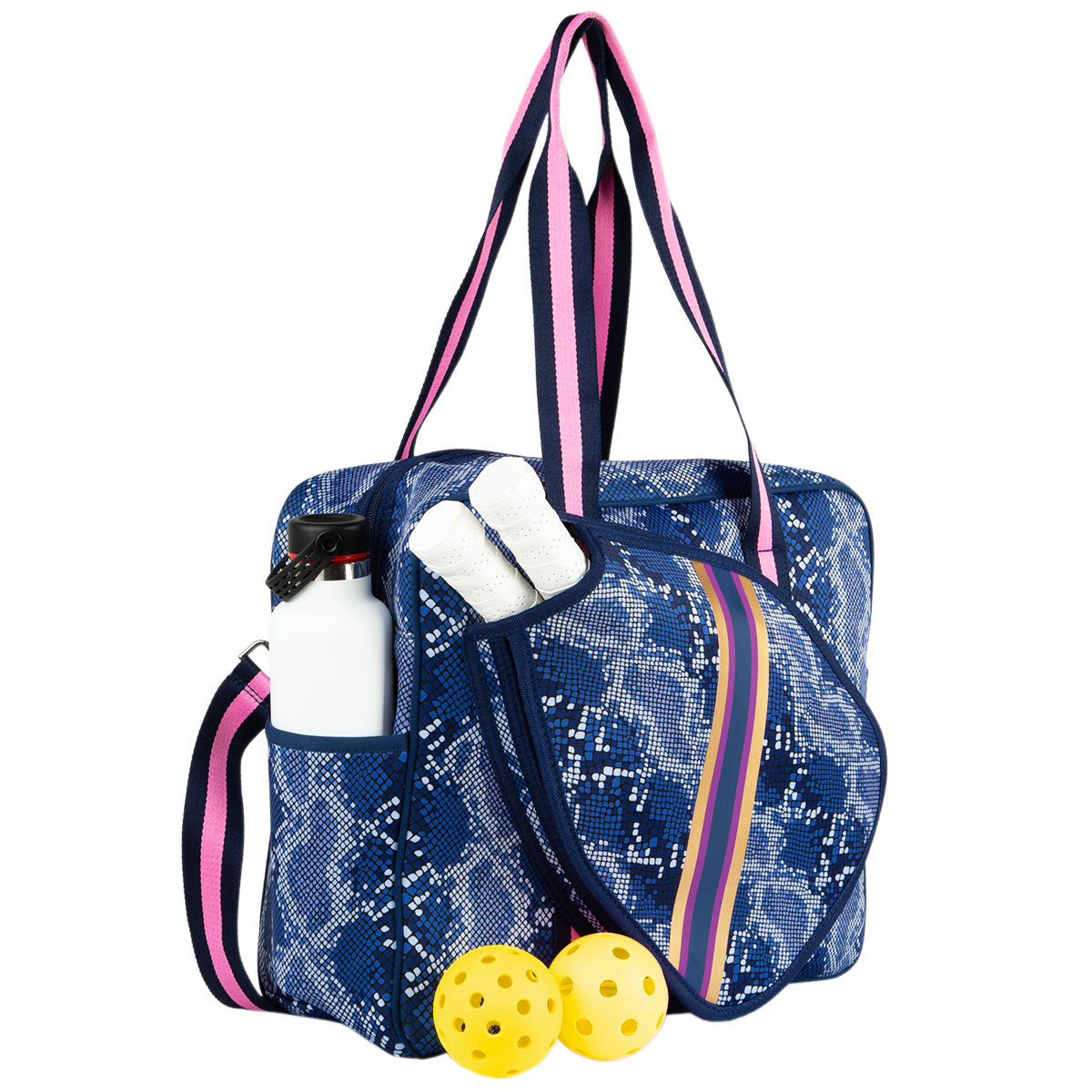 The Queen of the Court Brooklyn Pickleball Bag features a blue and white pattern, pink and navy straps, side pockets holding a water bottle and towels, and two yellow pickleballs by its colorful striped zipper paddle compartment.