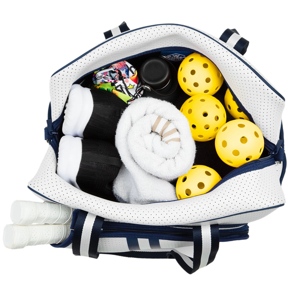 A Queen of the Court Brooklyn Pickleball Bag holds several yellow perforated pickleballs, a rolled white towel, black and white socks, a colorful pouch, a black water bottle, and three white paddle grips in its outer pocket.
