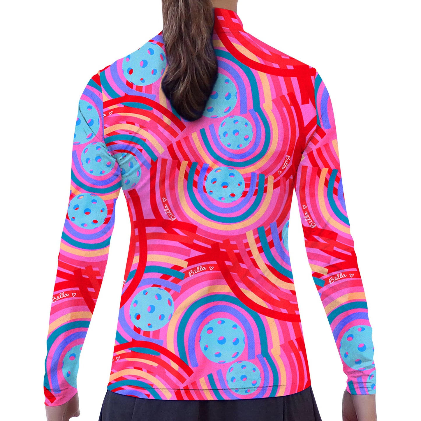 A woman faces away in the Pickleball Bella PB 1/4 Zip Long Sleeve Circle top, featuring vibrant geometric patterns in red, blue, pink, and purple. She pairs it with a black skirt; her brown hair is in a ponytail. White background.