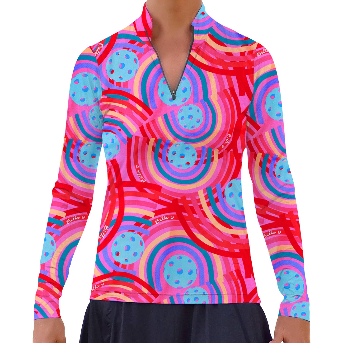 Someone wears the Pickleball Bella PB 1/4 Zip Long Sleeve Circle top, featuring swirling pink, red, and purple stripes with blue pickleball designs and white “pickle” text. A black skirt is visible; the person's face is not shown.