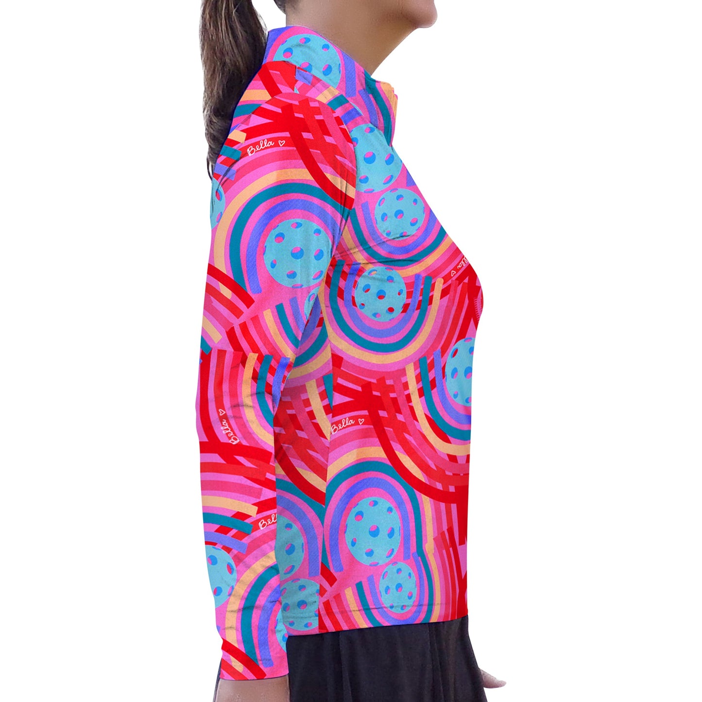 A person stands in profile wearing the Pickleball Bella PB 1/4 Zip Long Sleeve Circle, featuring a bold geometric pattern of red, blue, pink, and purple arcs and polka dots layered over a black skirt against a minimalist white background.