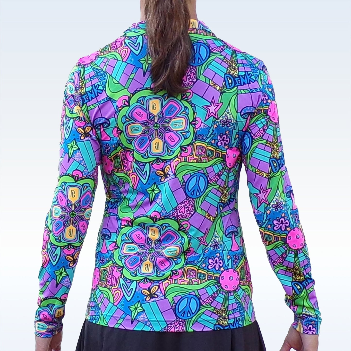 A person with long brown hair in a ponytail wears the Pickleball Bella PB 1/4 Zip Long Sleeve Groovy—a vibrant top with colorful psychedelic designs and UV protection, perfect for pickleball. The background is light blue.
