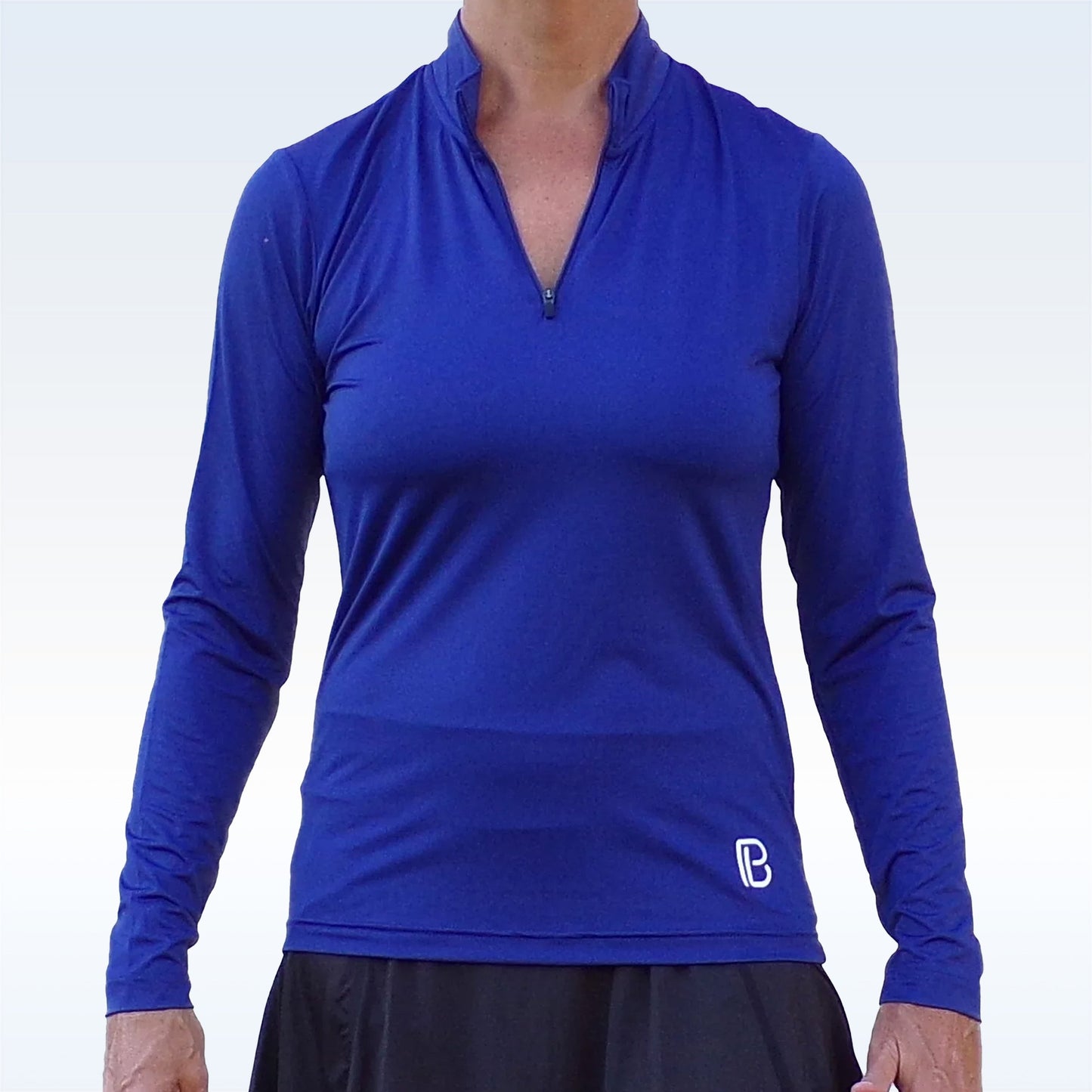 A person wears the Pickleball Bella PB 1/4 Zip Long Sleeve Navy pullover with a small white logo and a black skirt. The background is a pale gradient, and their face is not visible.