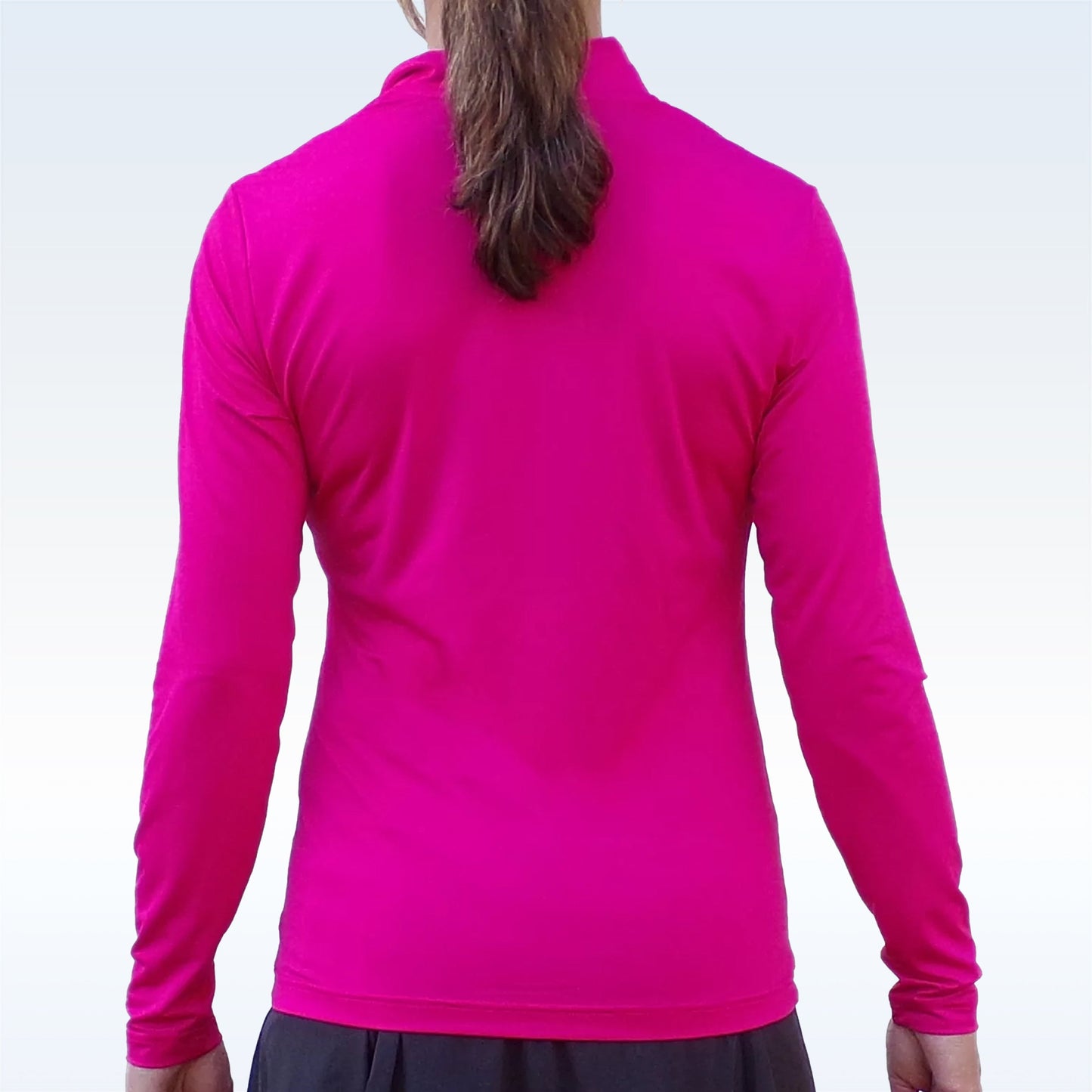 A person with long brown hair tied back, wearing the Pickleball Bella PB 1/4 Zip Long Sleeve Pink and a dark skirt, stands with relaxed arms against a plain light background.