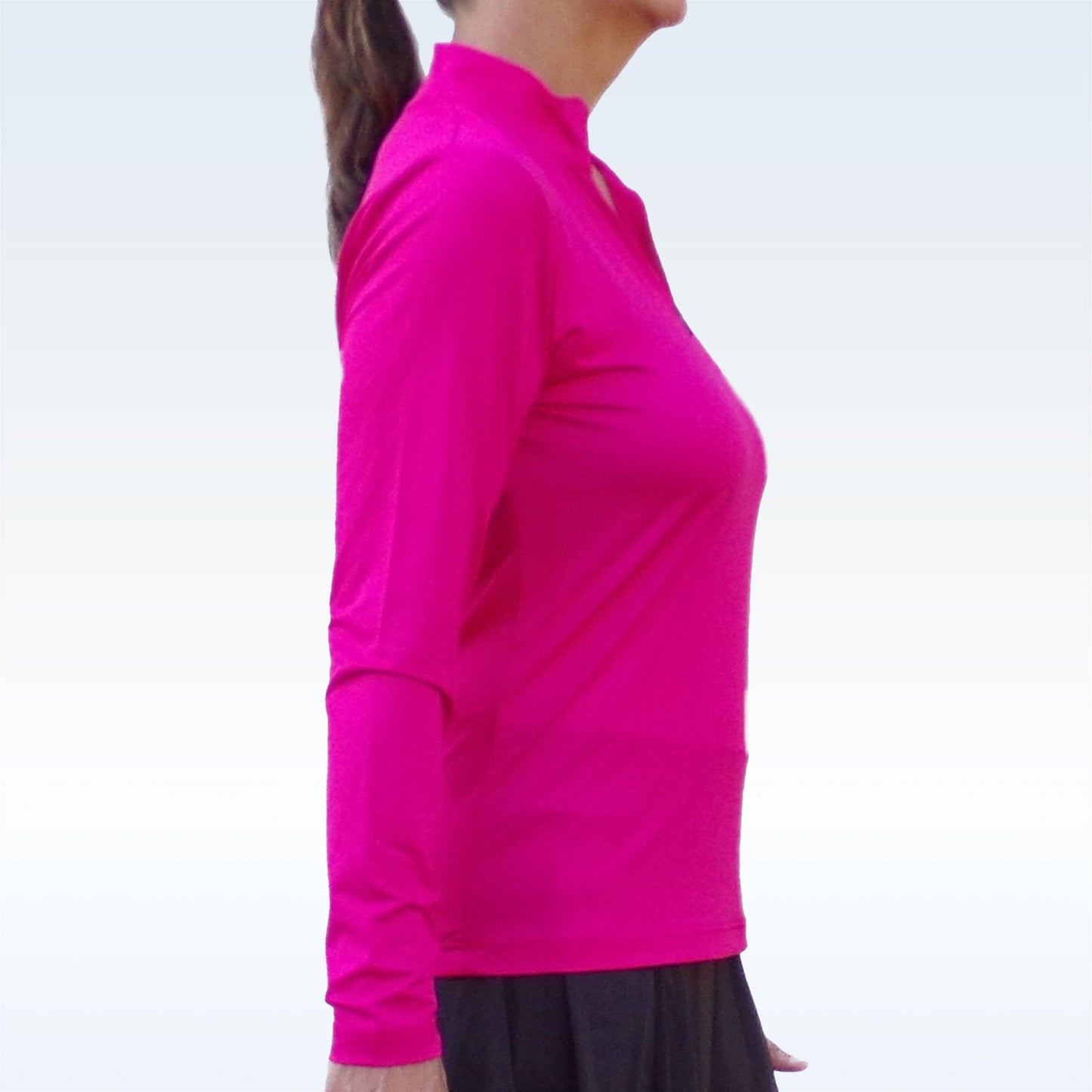 A woman with long brown hair in a ponytail is seen in profile wearing the Pickleball Bella PB 1/4 Zip Long Sleeve Pink against a light background. She pairs it with a black skirt; her face is partially visible and her posture upright.