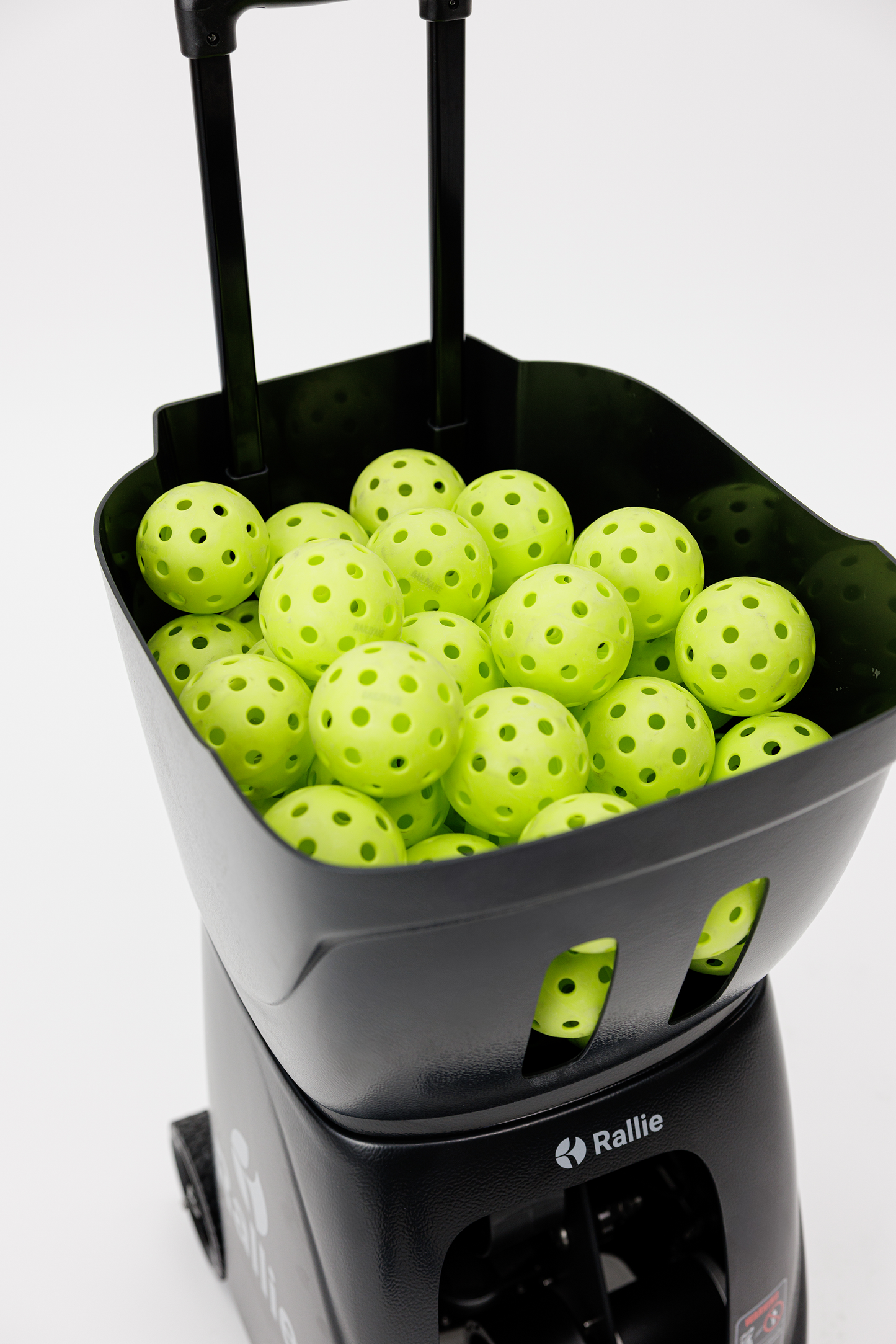 The Rallie Pickleball Machine - Midnight Black from Rallie Pickleball is shown with a black, wheeled cart filled with bright yellow-green perforated balls—ideal for training or use with the machine. The cart features a handle and is set against a white background.