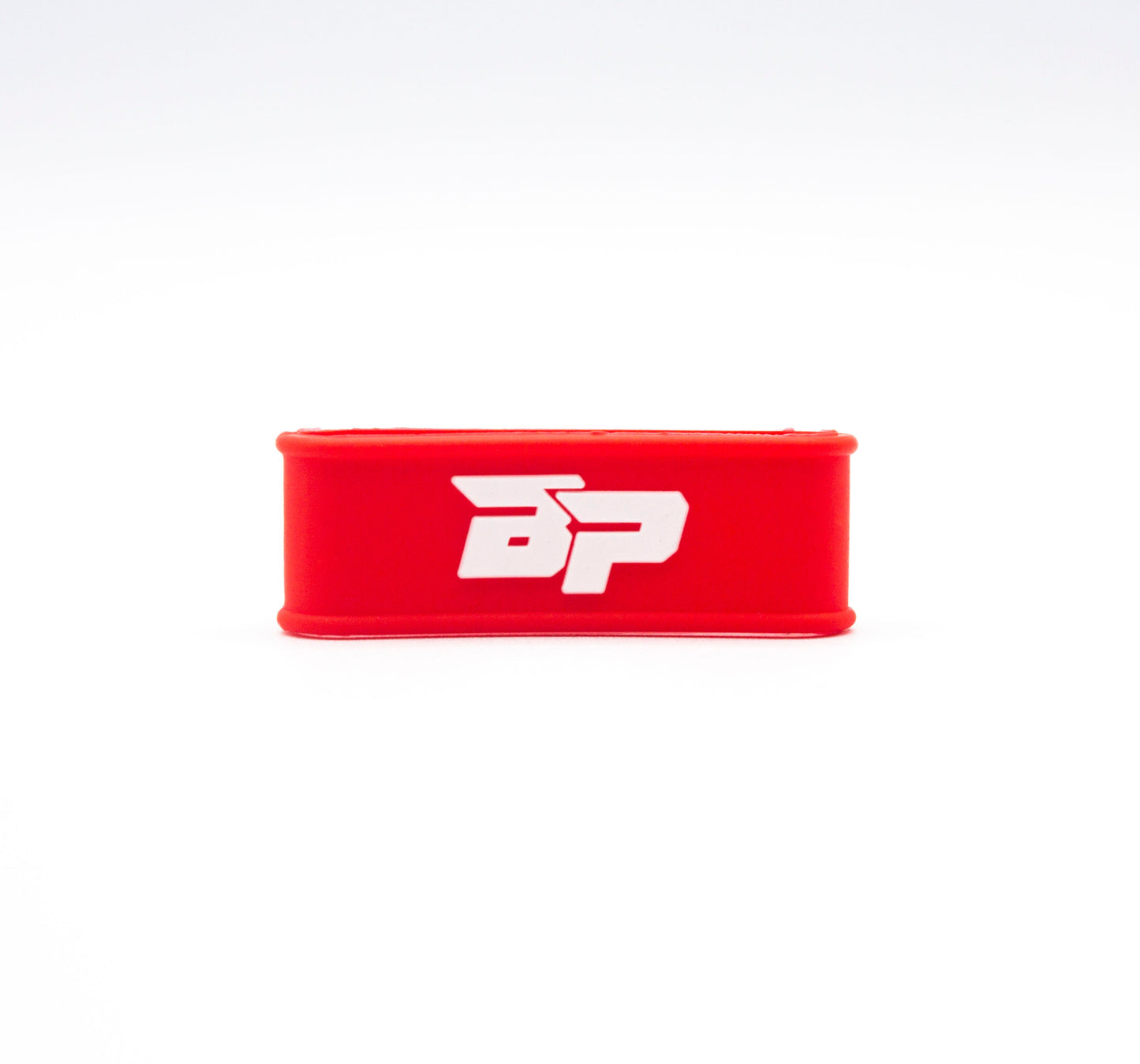 A red rectangular Paddle Band by Bodhi Performance rests on a white background, displaying bold white "BP" lettering. Designed for pickleball paddles, its smooth silicone edges and minimalist style provide both grip and function.