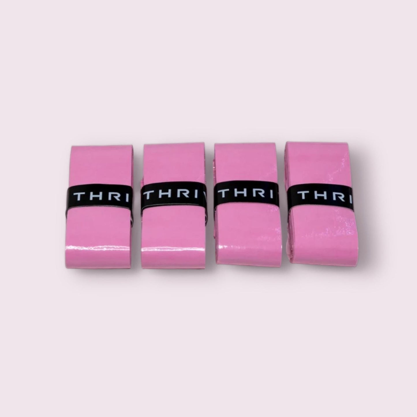 Four rectangular pink erasers, each wrapped in a black band reading “THRI,” are arranged in a row on a light pink background, resembling Thrive Pickleball's Overgrips (Super Tacky), known for unrivaled tackiness and durability.