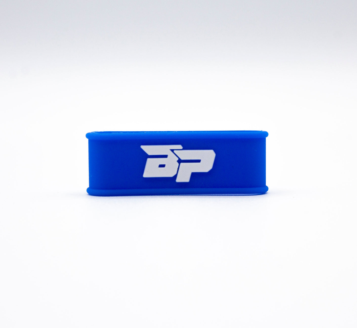 A blue rectangular silicone Paddle Band by Bodhi Performance is centered on a white background, featuring bold white "BP" letters on the front. Its smooth, minimalist design makes it an ideal pickleball paddle accessory.