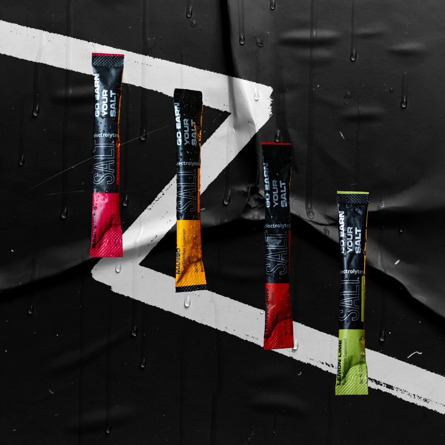 Four SALT Electrolytes Sample Kit packets—Lemon Lime, Strawberry, Mango, and Orange—stand vertically against a wet black background with bold white lines and water droplets for a fresh, moody effect.