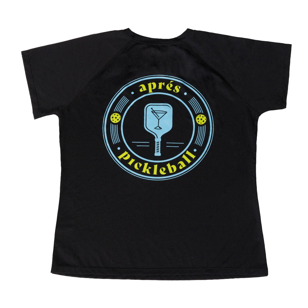 The Swinton Pickleball Women's Aprés Pickleball Performance Shirt is a black moisture-wicking tee with a circular back logo featuring a blue paddle, cocktail glass, yellow pickleballs, music notes, and “après pickleball” in blue and yellow.