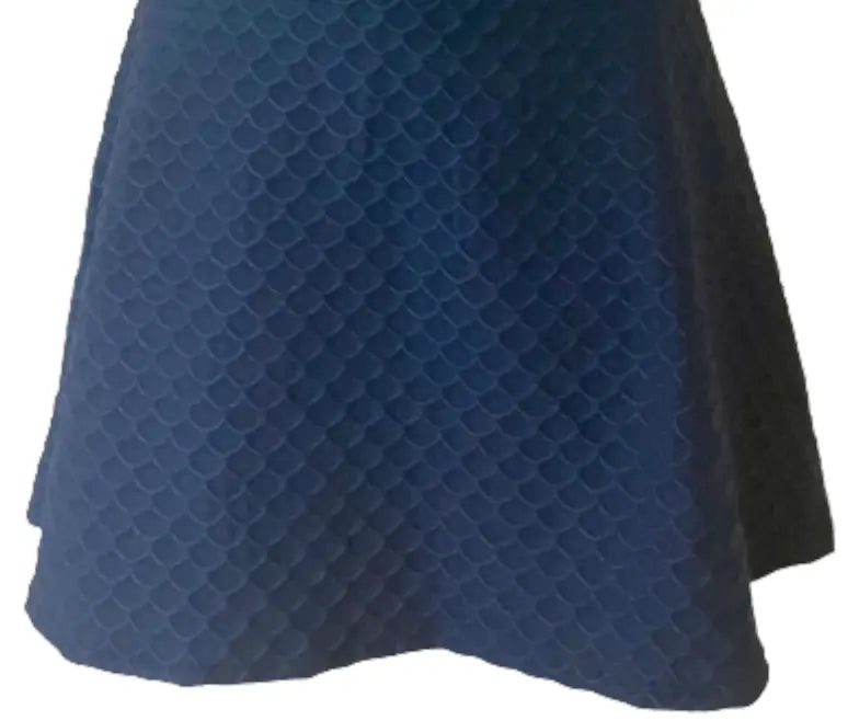 The Nola Navy Blue Scallop Skirt by Runway Athletics features a flared A-line silhouette, scale-inspired texture, knee-length uneven hem, and a moisture-wicking under-short for comfort on or off the court.