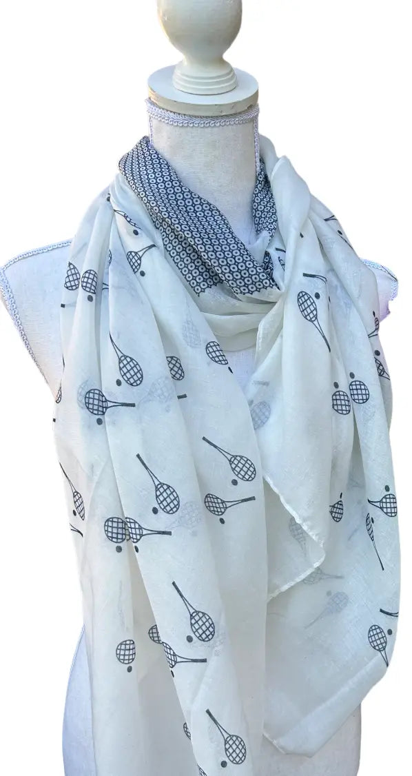 The Runway Athletics Racquet Time Sun Scarf/Wrap showcases a white fabric with black racket motifs and a darker geometric inner layer, offering a chic, layered look that doubles as sun protection on or off the court.