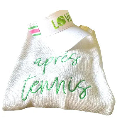 The Apres Tennis Sweater by Runway Athletics, a white crew neck with “après tennis” in green cursive, pairs perfectly with a striped visor featuring green, pink, and white stripes plus bold green “LOVE”—a great gift for tennis fans.