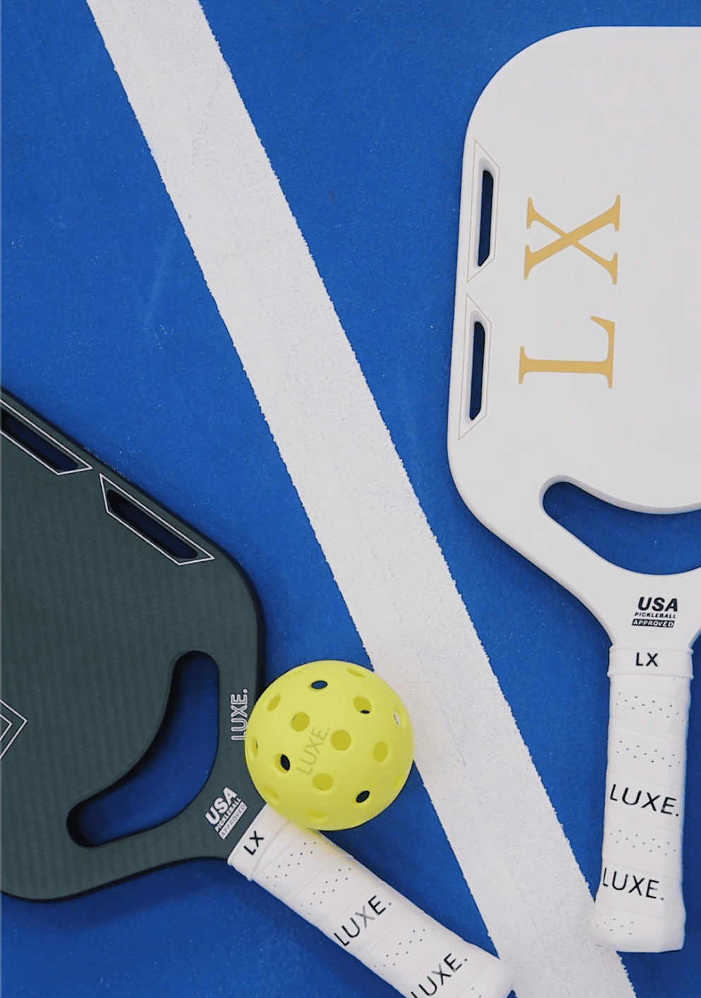 Two lightweight LX pickleball paddles by LUXE Pickleball—one black, one white, both with USA LUXE grip tape and USA Pickleball approval—plus a yellow ball, rest on a blue court by a white line.