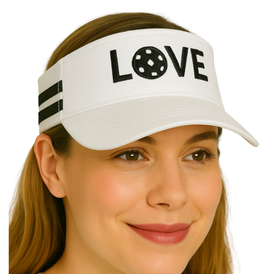 A woman with light brown hair wears the Runway Athletics Pickleball Visor - White & Black, featuring two black stripes and "LOVE" on the front, where a black pickleball forms the O. She smiles softly, looking slightly to the side.