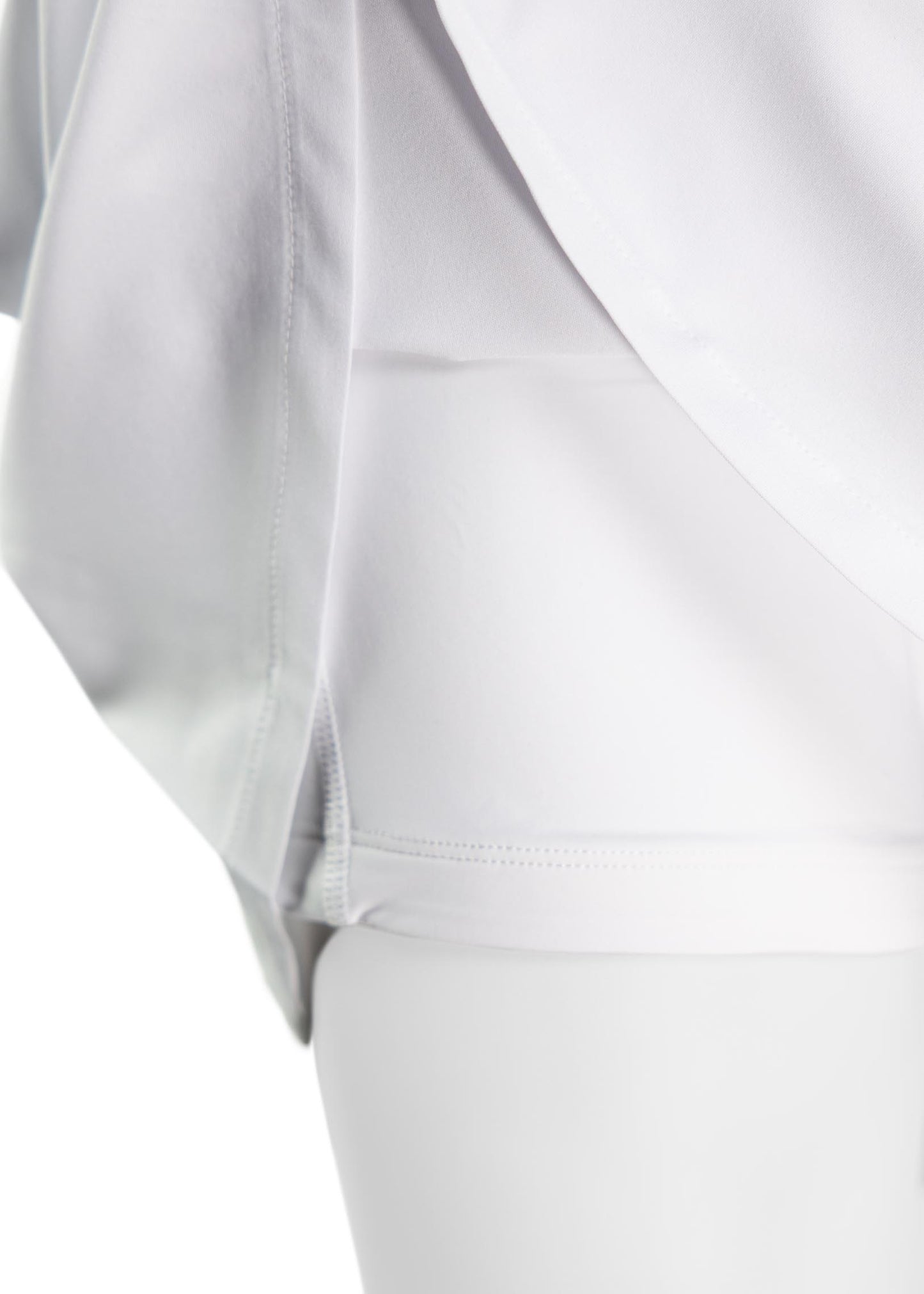 Close-up of a person wearing the TMPR Performance Mid-Rise Skort by TMPR Sports, showcasing its smooth seams and layered design with a white draped overlay and built-in fitted shorts underneath.