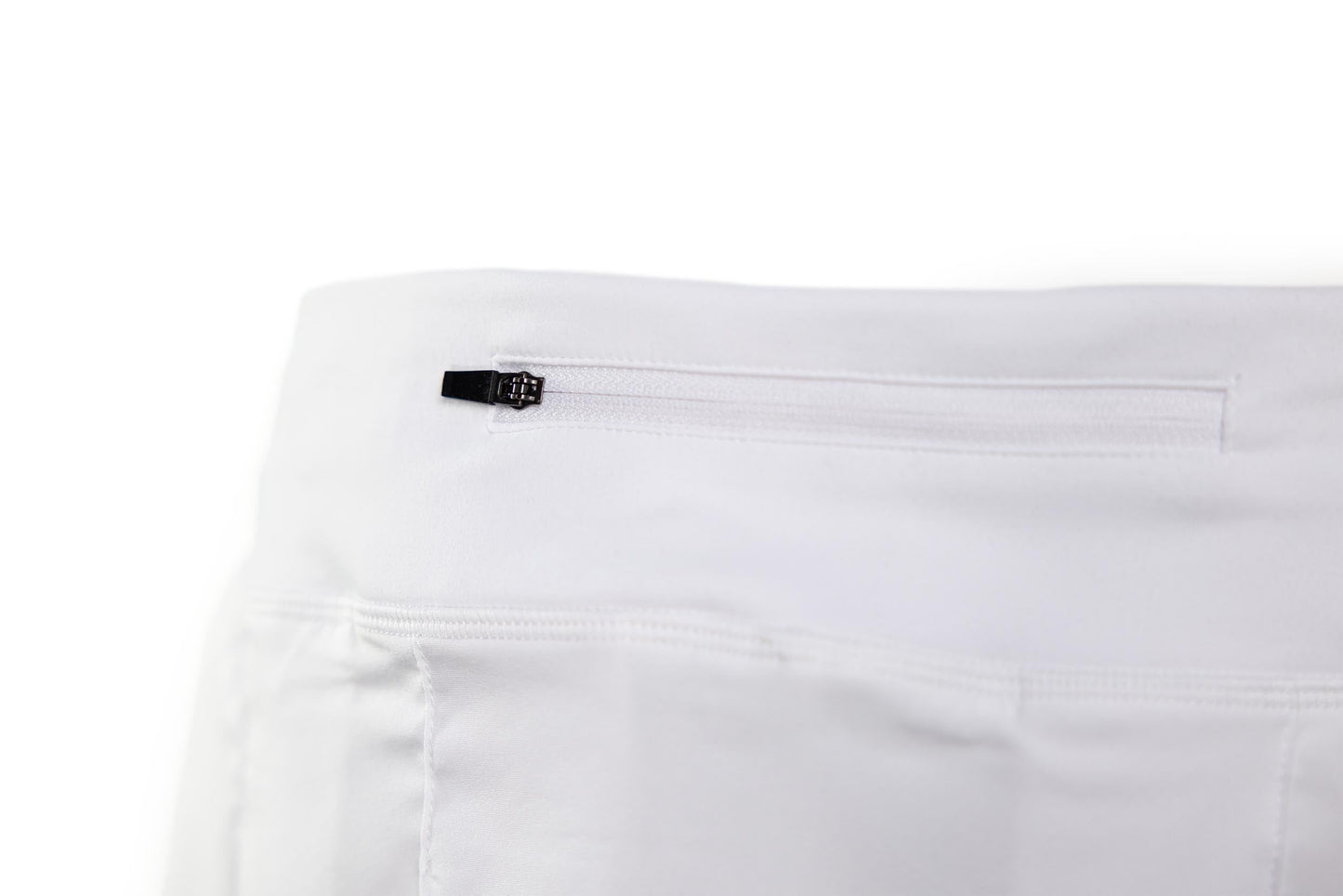 Close-up of the TMPR Sports Performance Mid-Rise Skort in white, showing a horizontal zippered pocket with a black pull near the waistband. Plain white background highlights the skort’s fabric and stitching details.