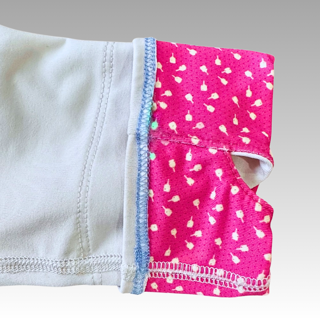 A close-up of the Soleil Tech Shirt by Playly Store shows white fabric joined to pink floral fabric with a white and blue overlock stitch. The breathable material enhances comfort, set against a smooth grey gradient background.