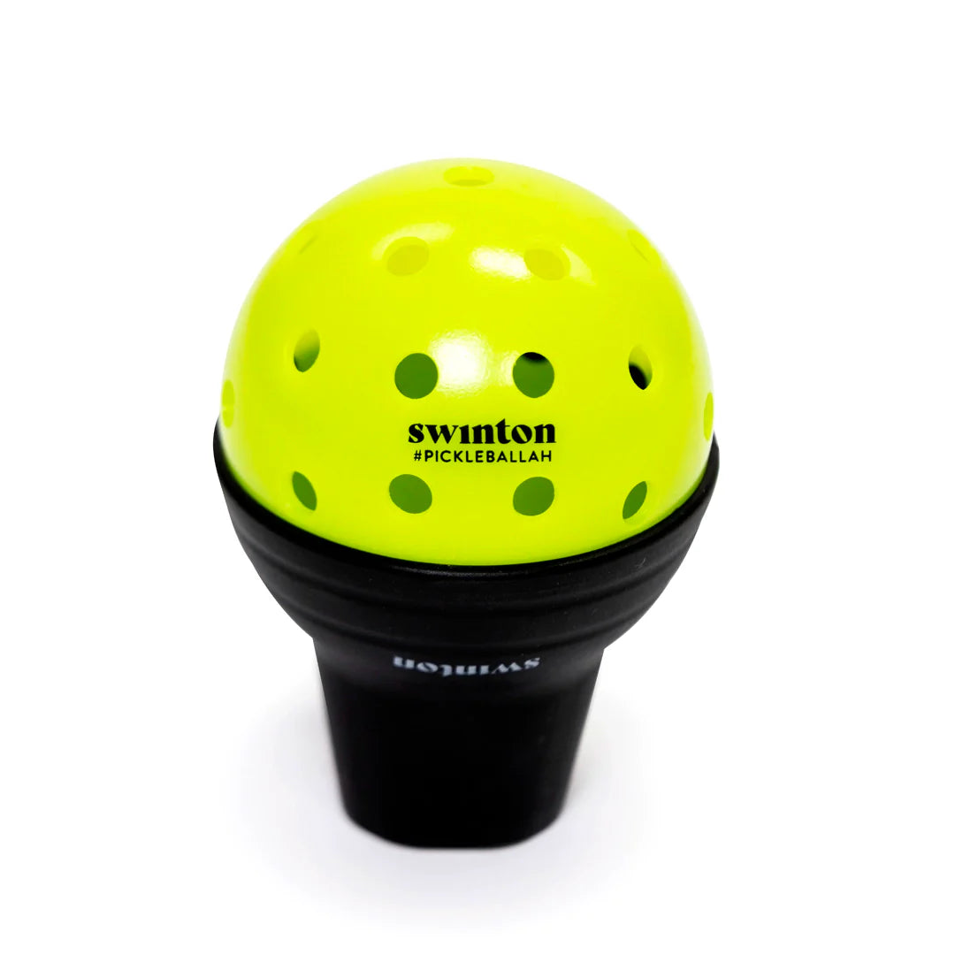 A bright yellow perforated Swinton Pickleball ball (#PICKLEBALL4H) sits on a black Suck Up ball retriever, both displayed against a plain white background.