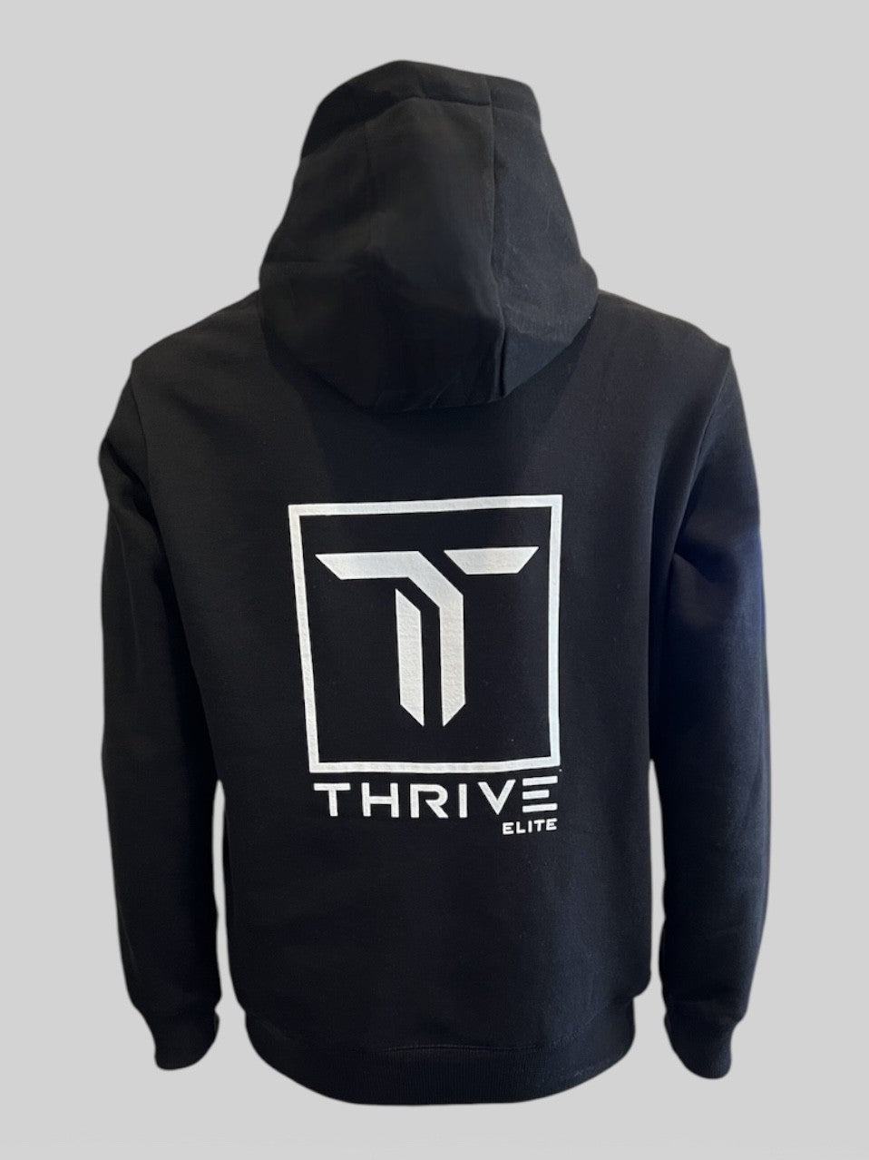 The Thrive Pickleball Thrive Elite Hoodie in black, shown from the back, features a large white geometric logo inside a square with "THRIVE" in bold and "ELITE" below on recycled polyester, set against a plain gray background.