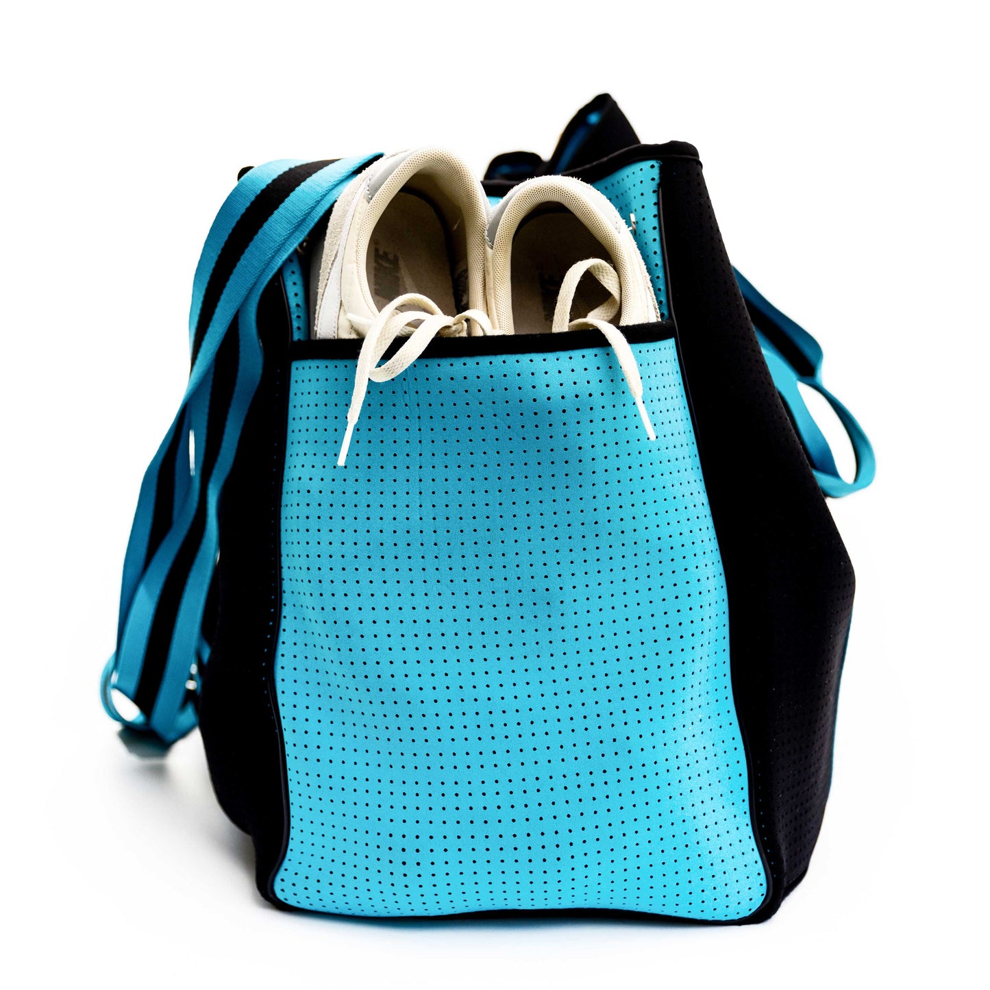 The Swinton Pickleball XL Pickleball Tote Bag - Black sits upright on a plain white background, its blue perforated front pocket holding white sneakers. A wide blue-and-black striped shoulder strap completes the look.
