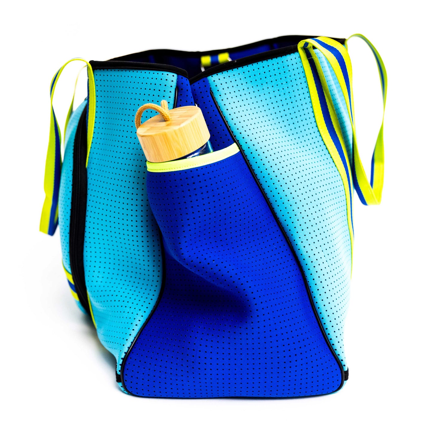 The Swinton Pickleball XL Pickleball Tote Bag - Blue stands upright with yellow striped handles. A reusable glass water bottle with a bamboo lid is tucked into its front pocket, set against a plain white background.