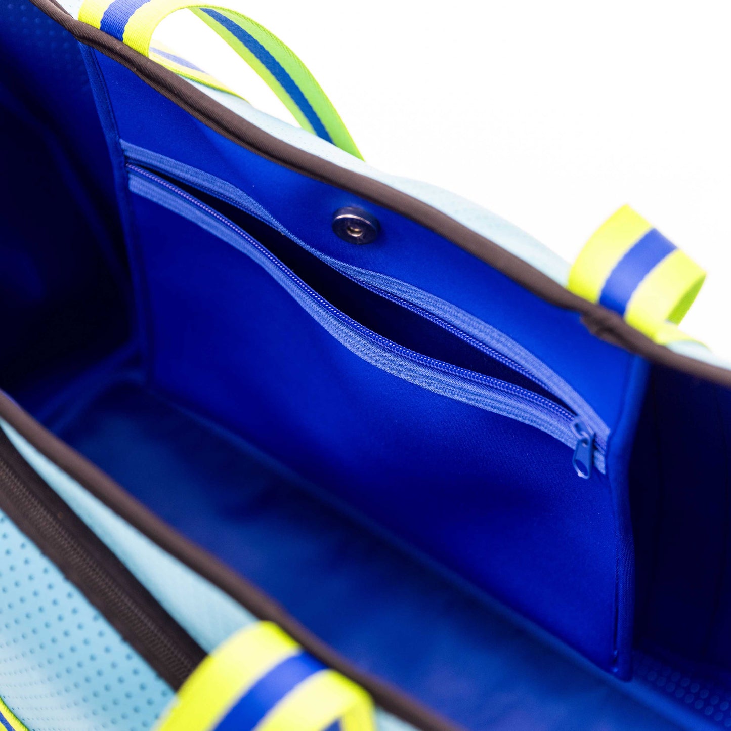 Close-up of the Swinton Pickleball XL Pickleball Tote Bag - Blue, featuring a zippered pocket, snap button, neon yellow and green striped handles, blue lining, and light blue sides against a white background.