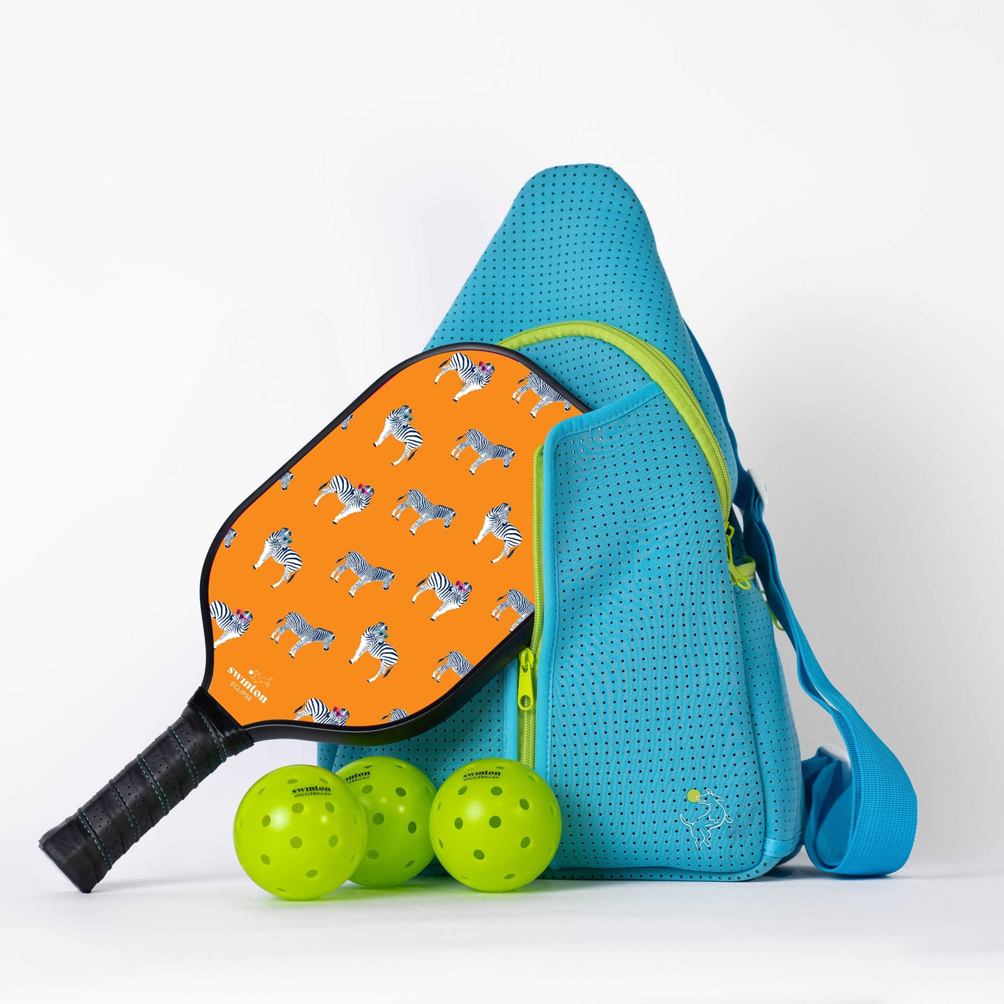 A blue Swinton Pickleball sling bag stands upright with an orange, zebra-themed paddle in front. Three yellow-green pickleballs sit nearby, all part of the Pickleball Starter Bundle - Blue on a white background.