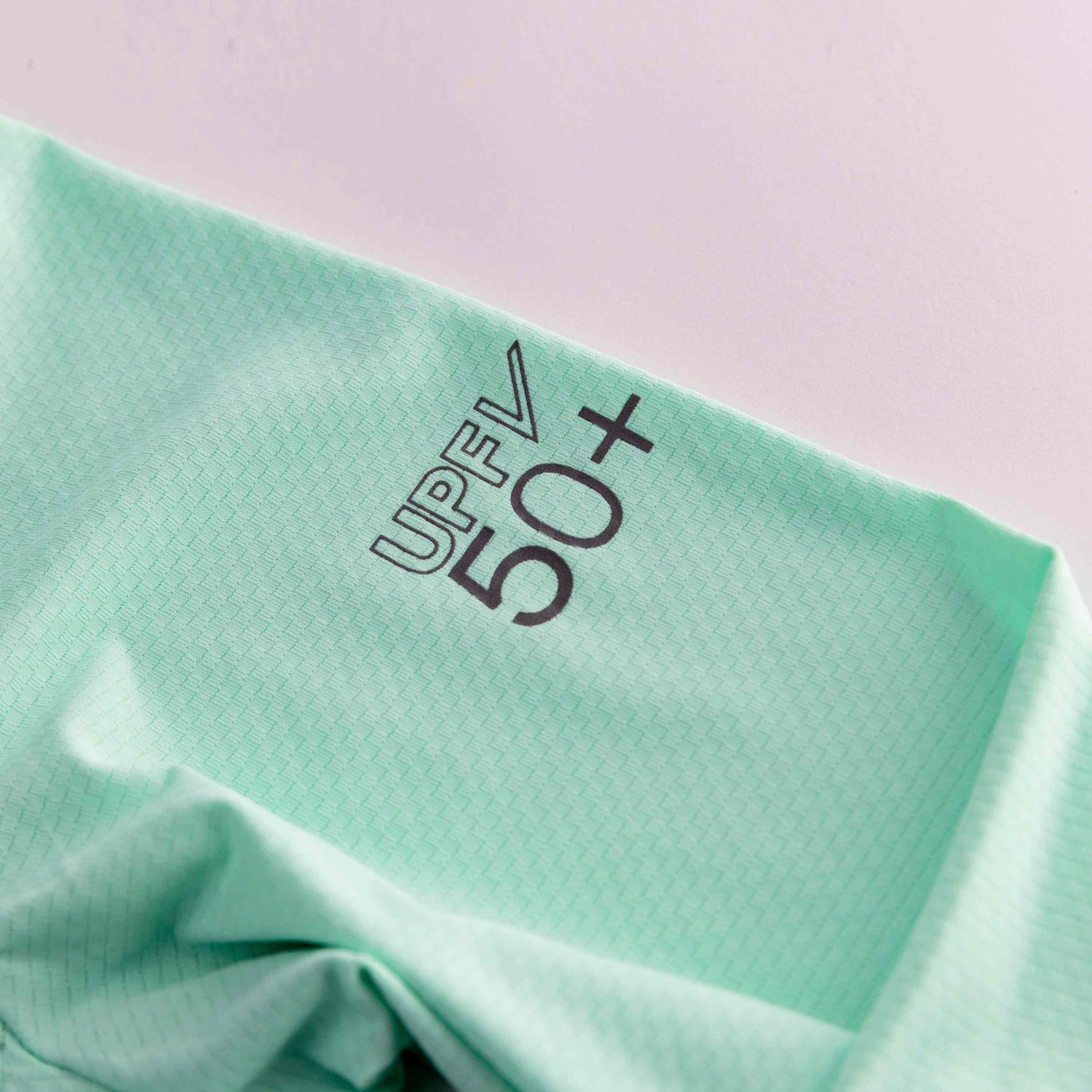 A close-up of Swinton Pickleball’s Mint Zip-Front Sun Hoodie reveals lightweight, breathable fabric with a subtle grid pattern and bold "UPF 50+," highlighting excellent UV protection and a smooth, slightly wrinkled surface.
