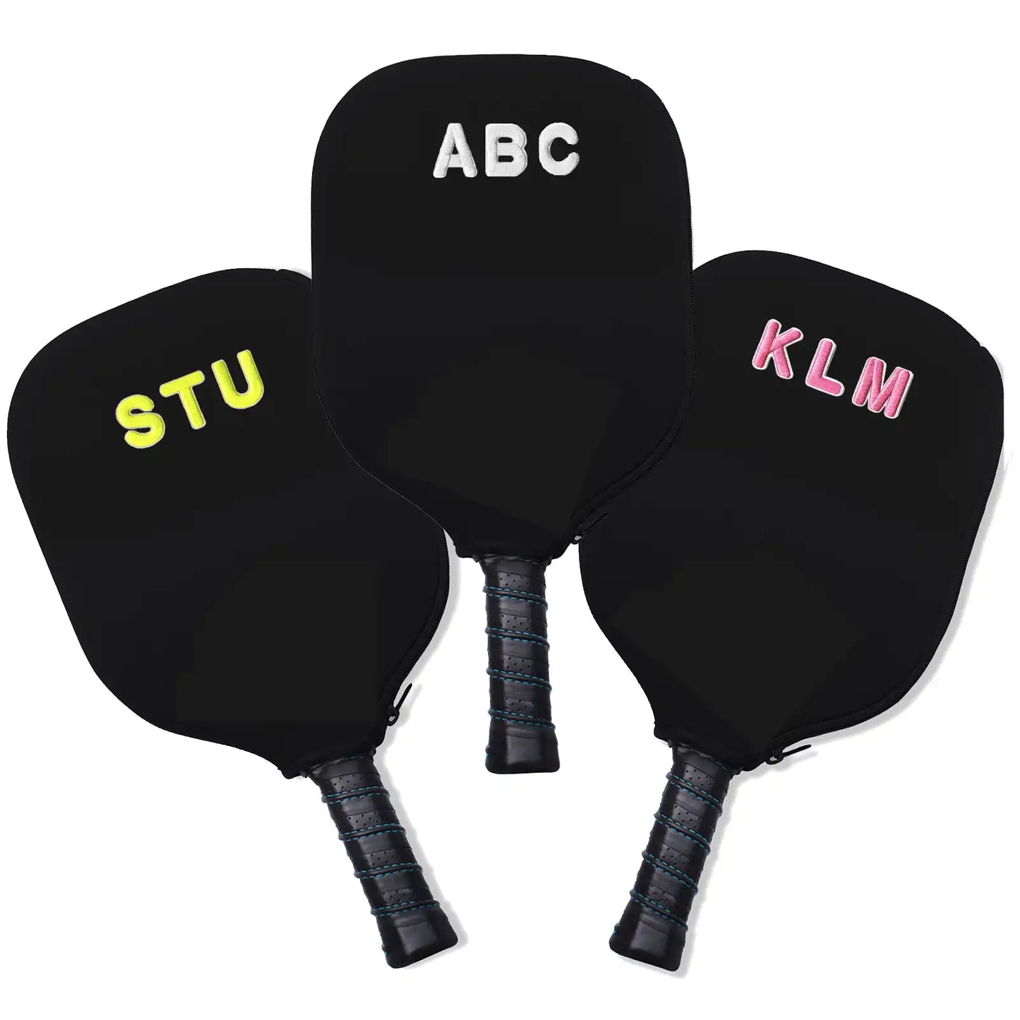 Three black Swinton Pickleball paddle covers for the Eclipse Island Vibes Pickleball Paddle are shown, each with 3D letters—ABC (white), STU (yellow), and KLM (pink)—and handles wrapped in black grip tape pointing downward.