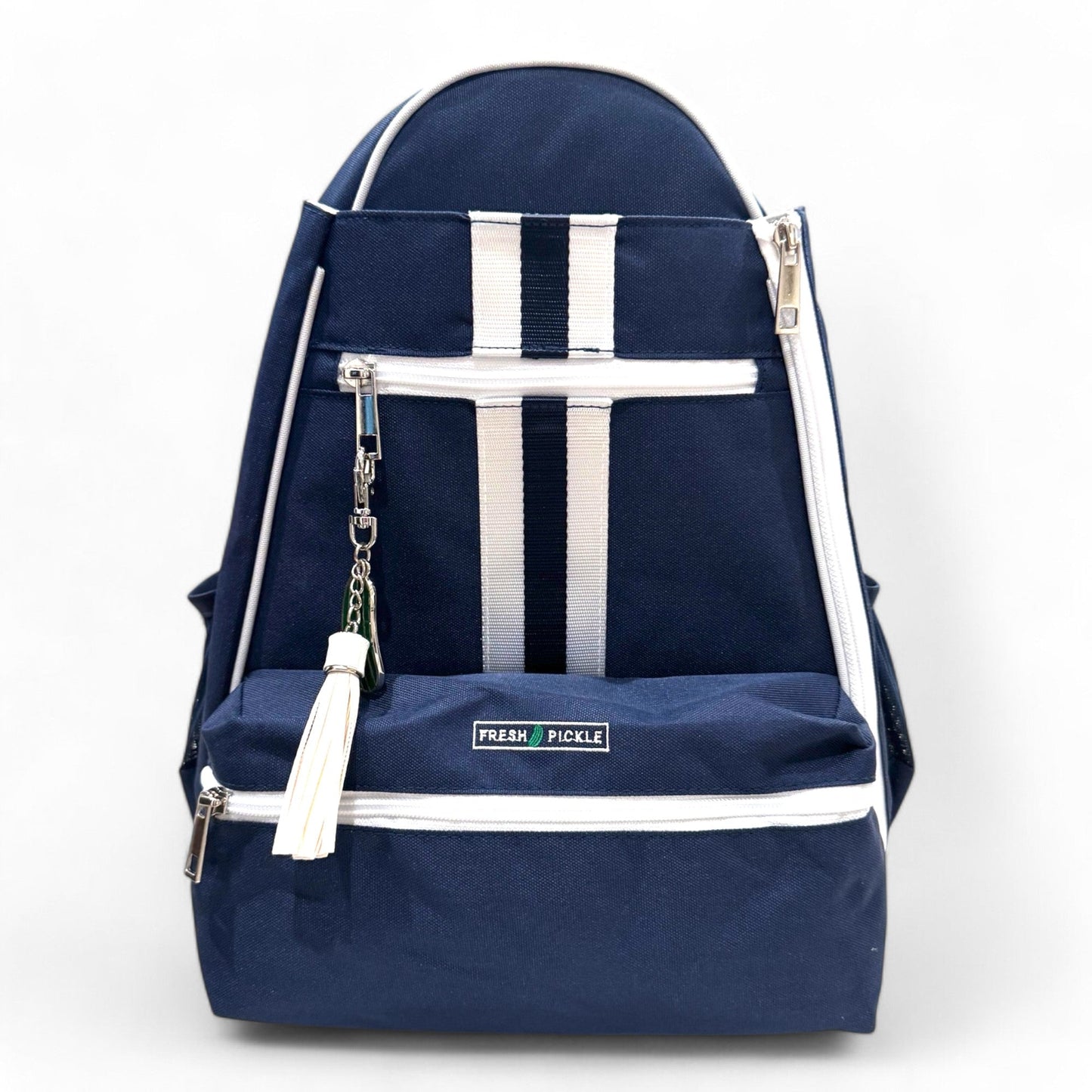 The Fresh Pickle Teddi Pickleball Backpack is a stylish navy blue, hands-free bag with white zippers, vertical stripes, front pocket, white tassel keychain, and “FRESH PICKLE” label. Ideal for daily use or as your pickleball backpack. Plain white background.