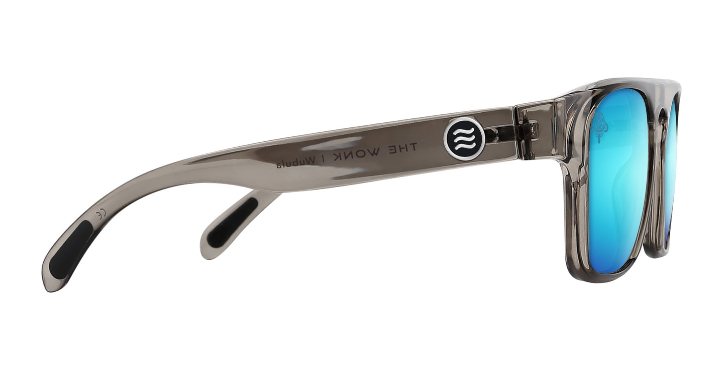 Side view of translucent gray polarized sunglasses, the Wubula by Neven Eyewear, featuring thick frames, blue mirrored lenses, and a circular logo with two wavy lines. “Neven Eyewear” appears in black on the inner side of the left arm.