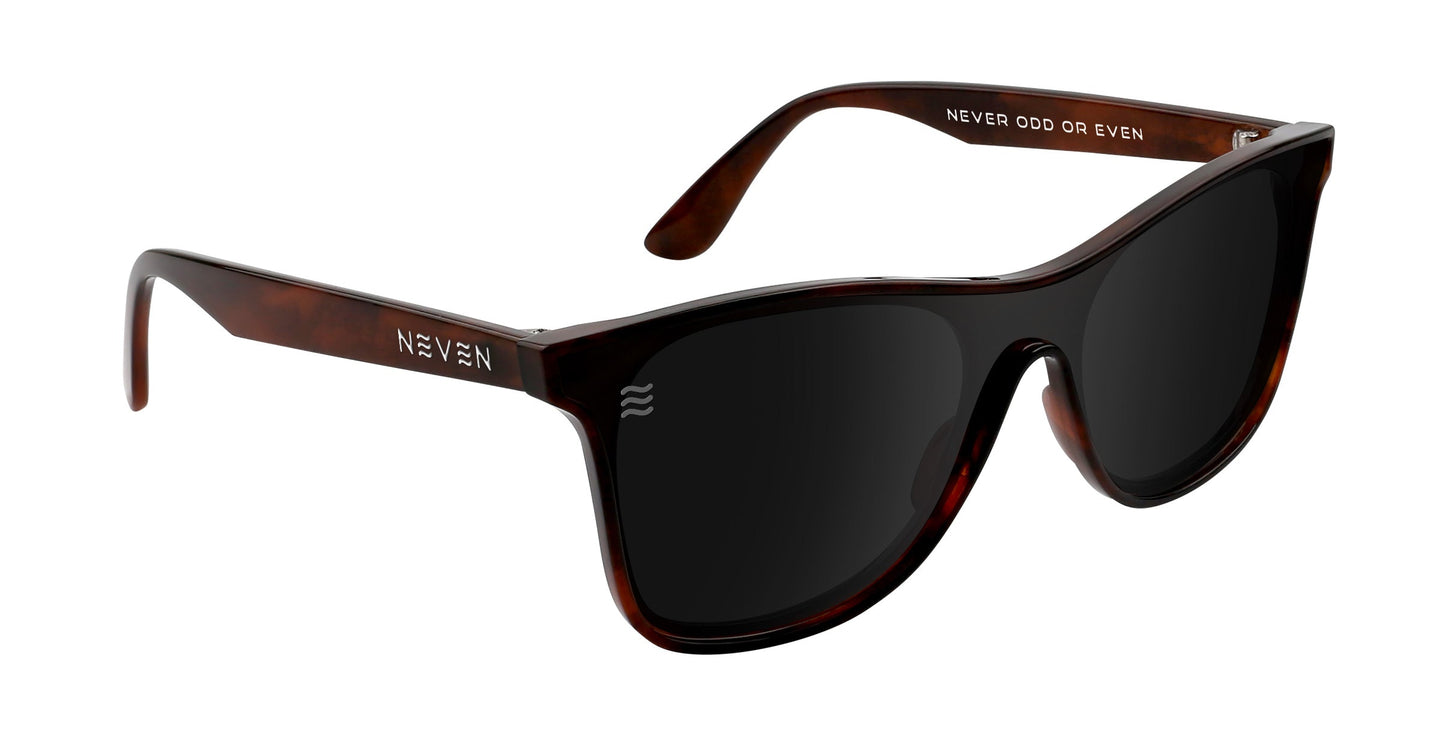 The Warlock by Neven Eyewear features oversized, dark tortoiseshell shield frames. "NEVEN" decorates the left temple and "NEVER ODD OR EVEN" the inside right. Black, polarized UV400 lenses are slightly reflective for stylish protection.