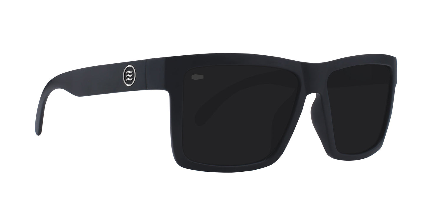 Neven Eyewear’s Lowrider sunglasses feature a black matte finish, thick rectangular frames, dark lenses, and a circular wavy-line logo on the left temple. This modern, sporty design draws inspiration from vintage motorcycle eyewear.